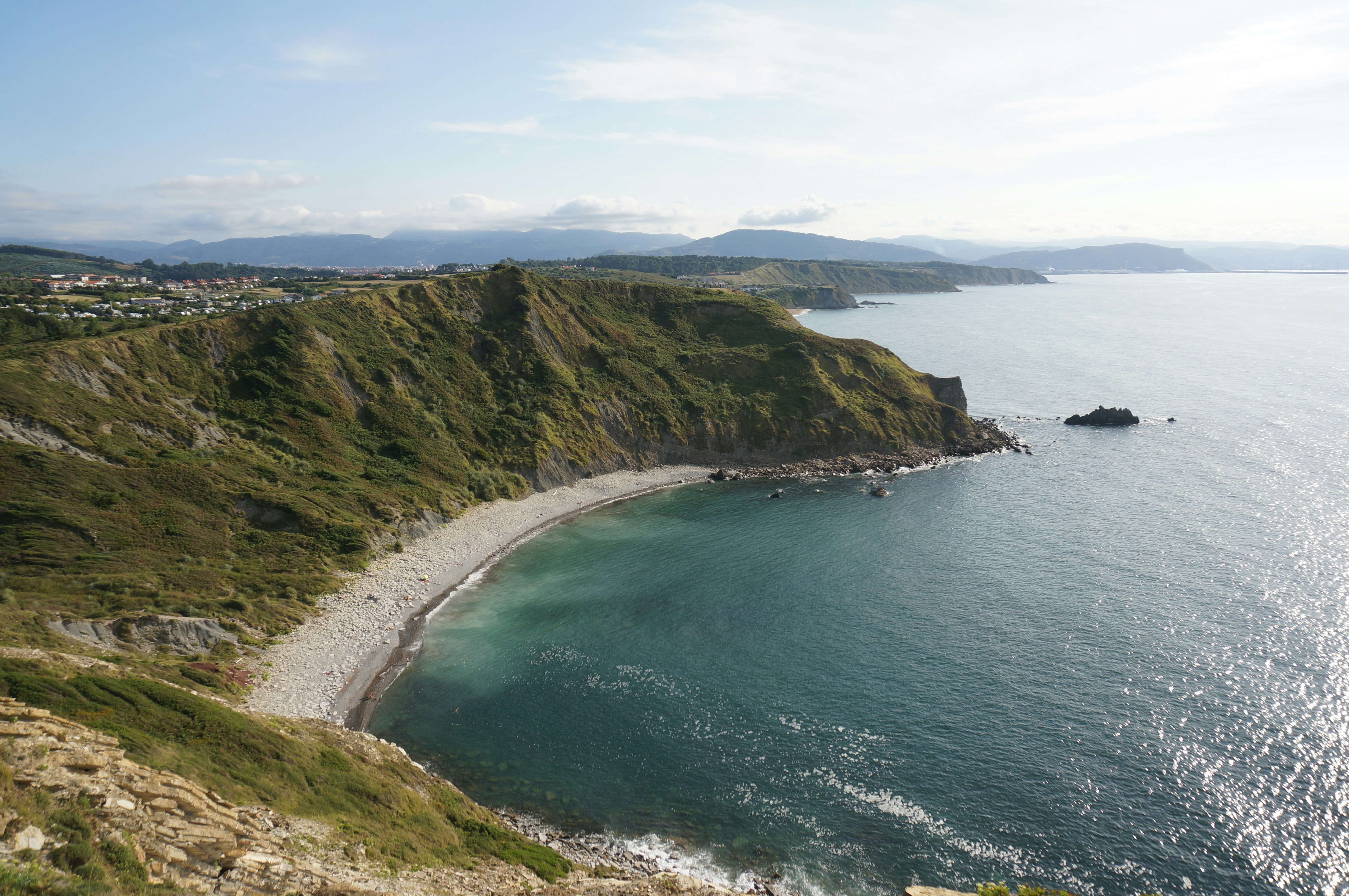 A rocky coastline with green cliffs curving around a small pebble beach