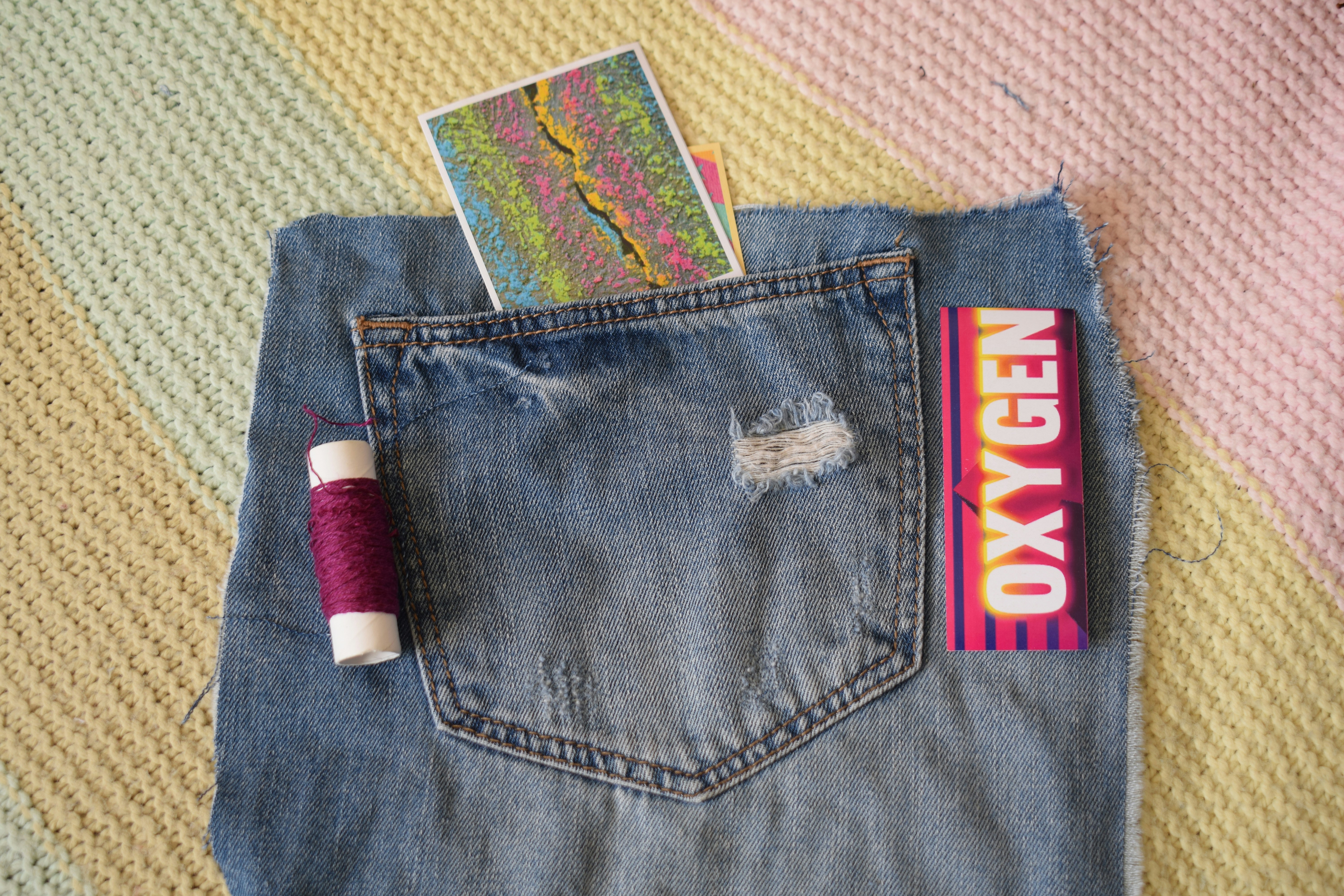 A denim pocket containing a colorful card, beside purple thread and an Oxygen sign