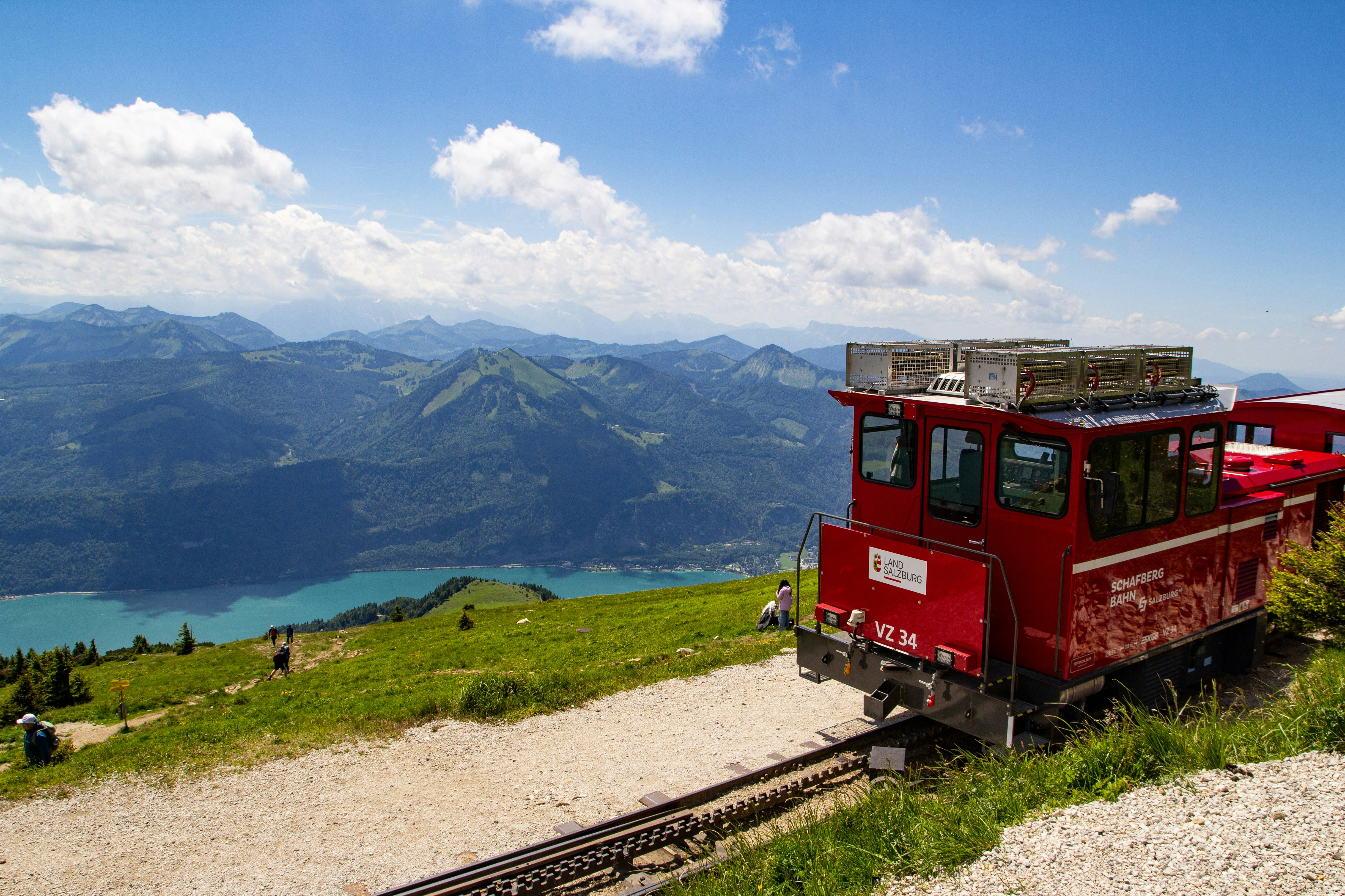 Kereta roda gigi Schafbergbahn merah di jalur pegunungan yang menghadap danau biru