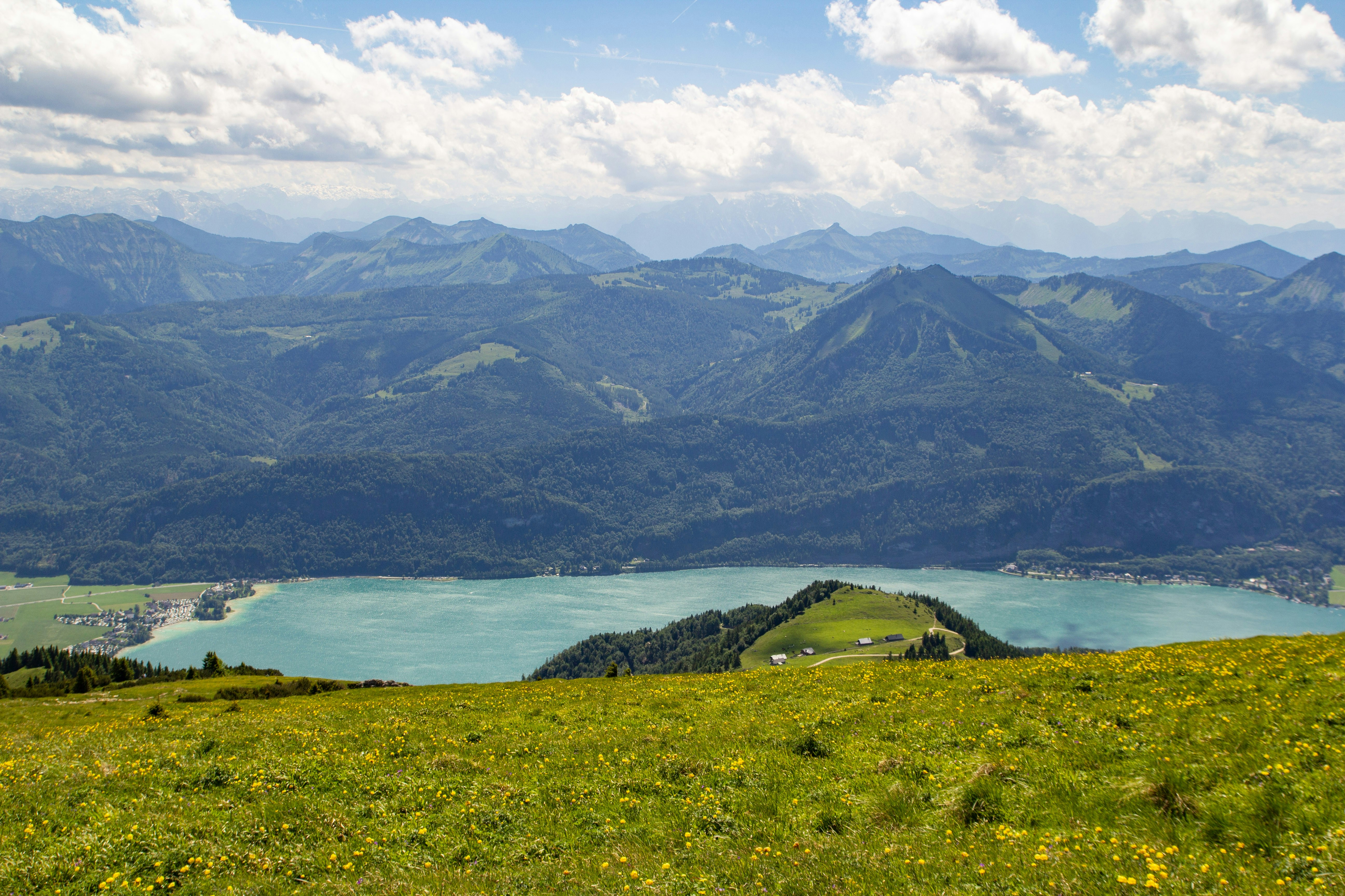 Danau biru kehijauan dikelilingi pegunungan hijau di bawah langit biru dengan awan