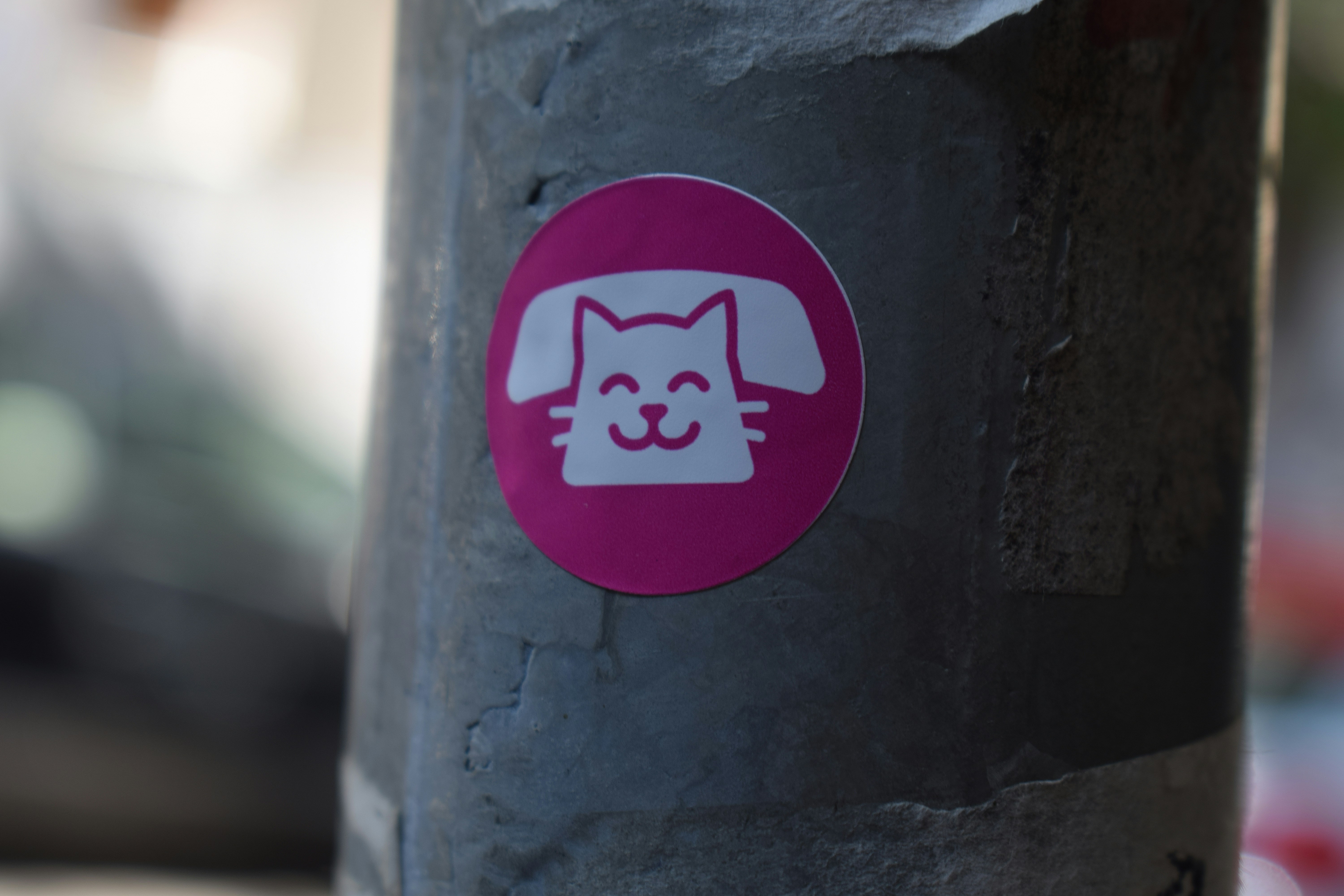A circular pink sticker with a white cat and telephone icon on a pole