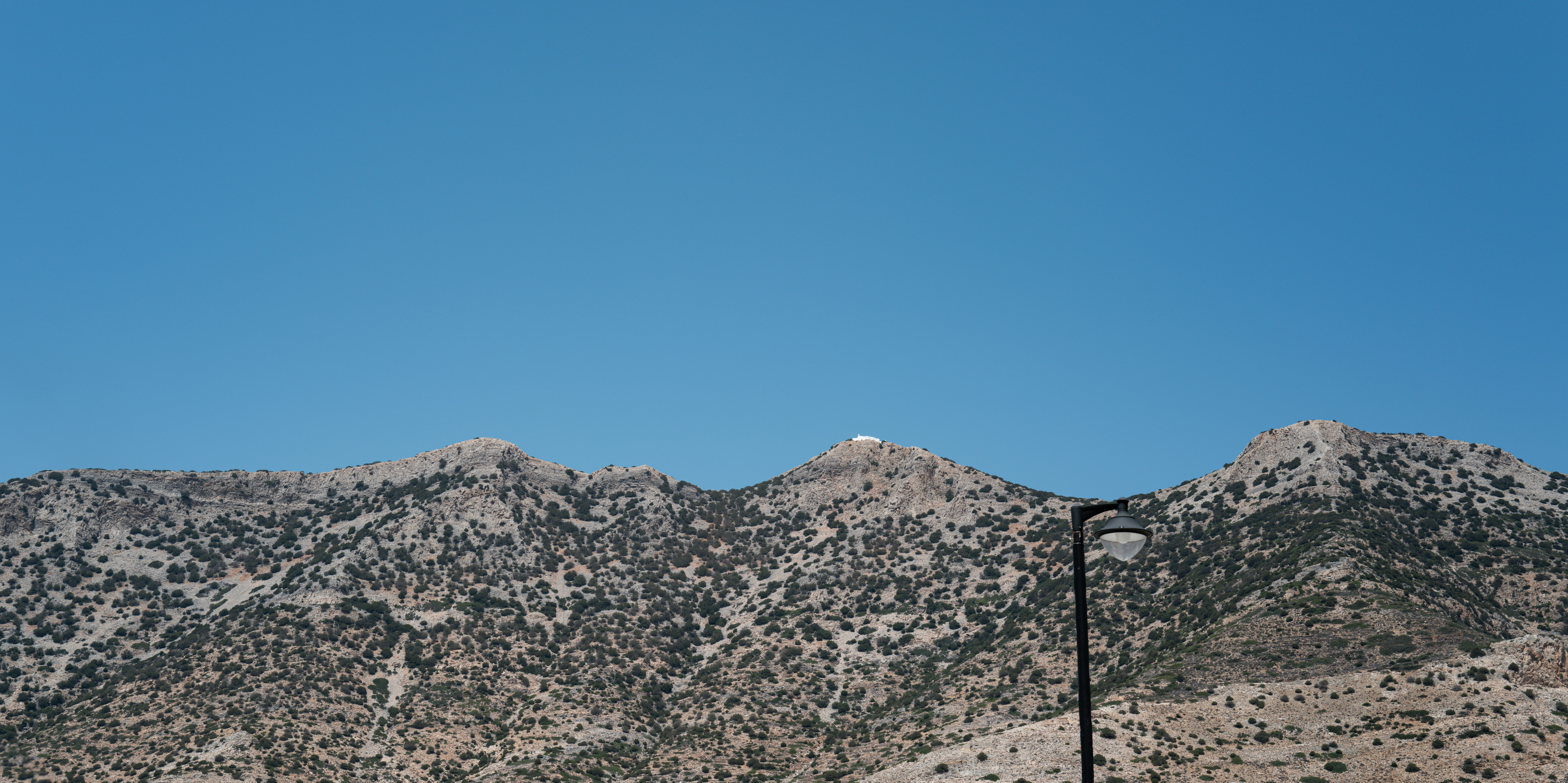 A rocky mountain range with sparse vegetation under a clear blue sky