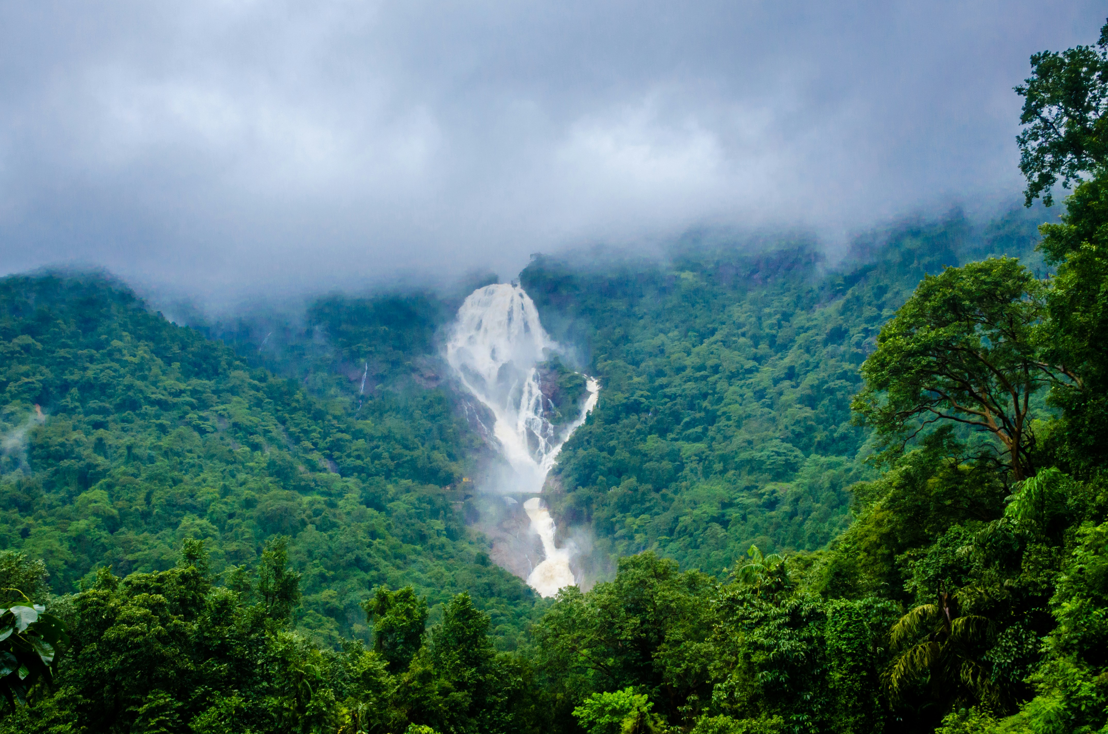 A large waterfall cascading down a lush green mountain slope under cloudy skies