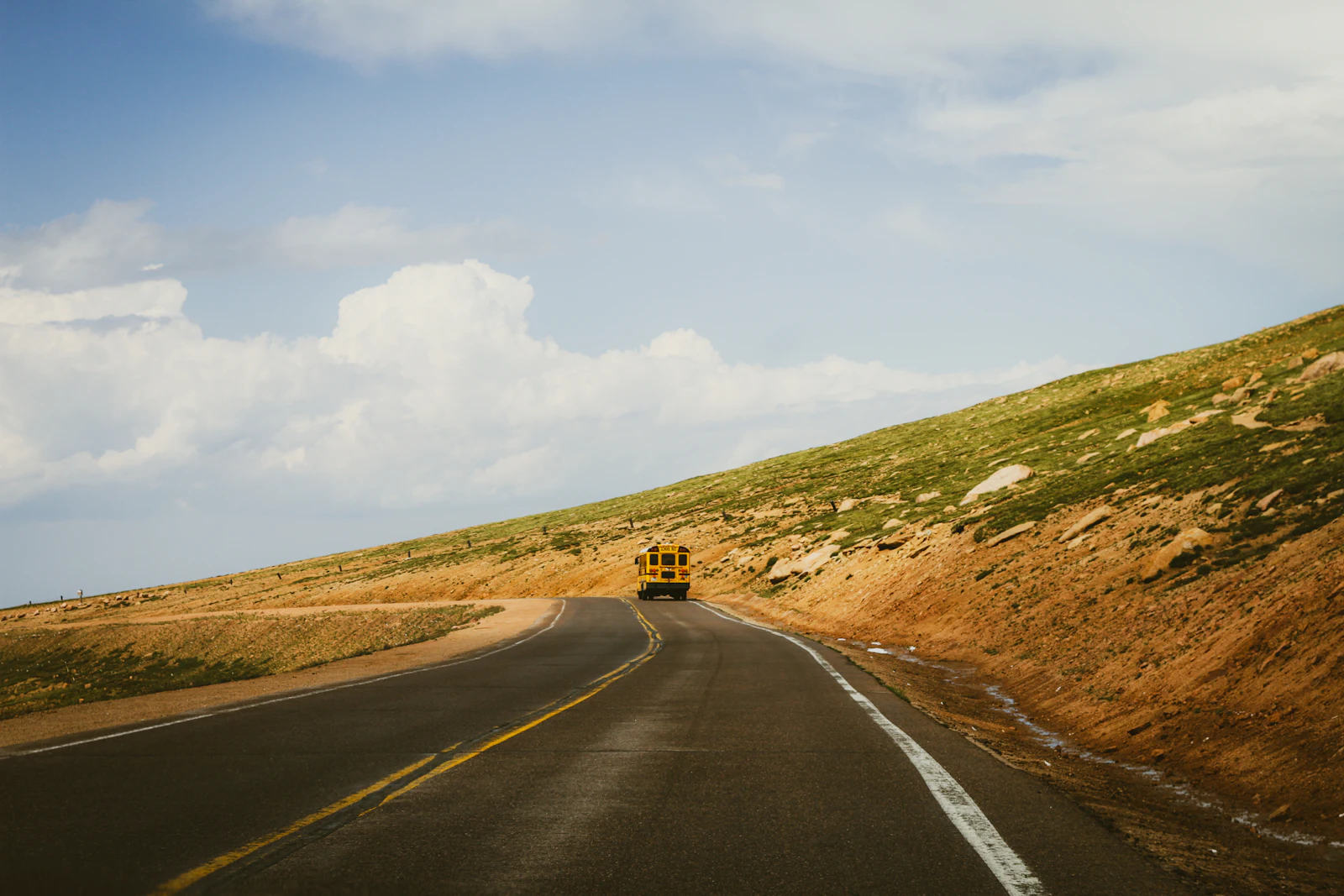 A yellow school bus on a winding road through a grassy hillside