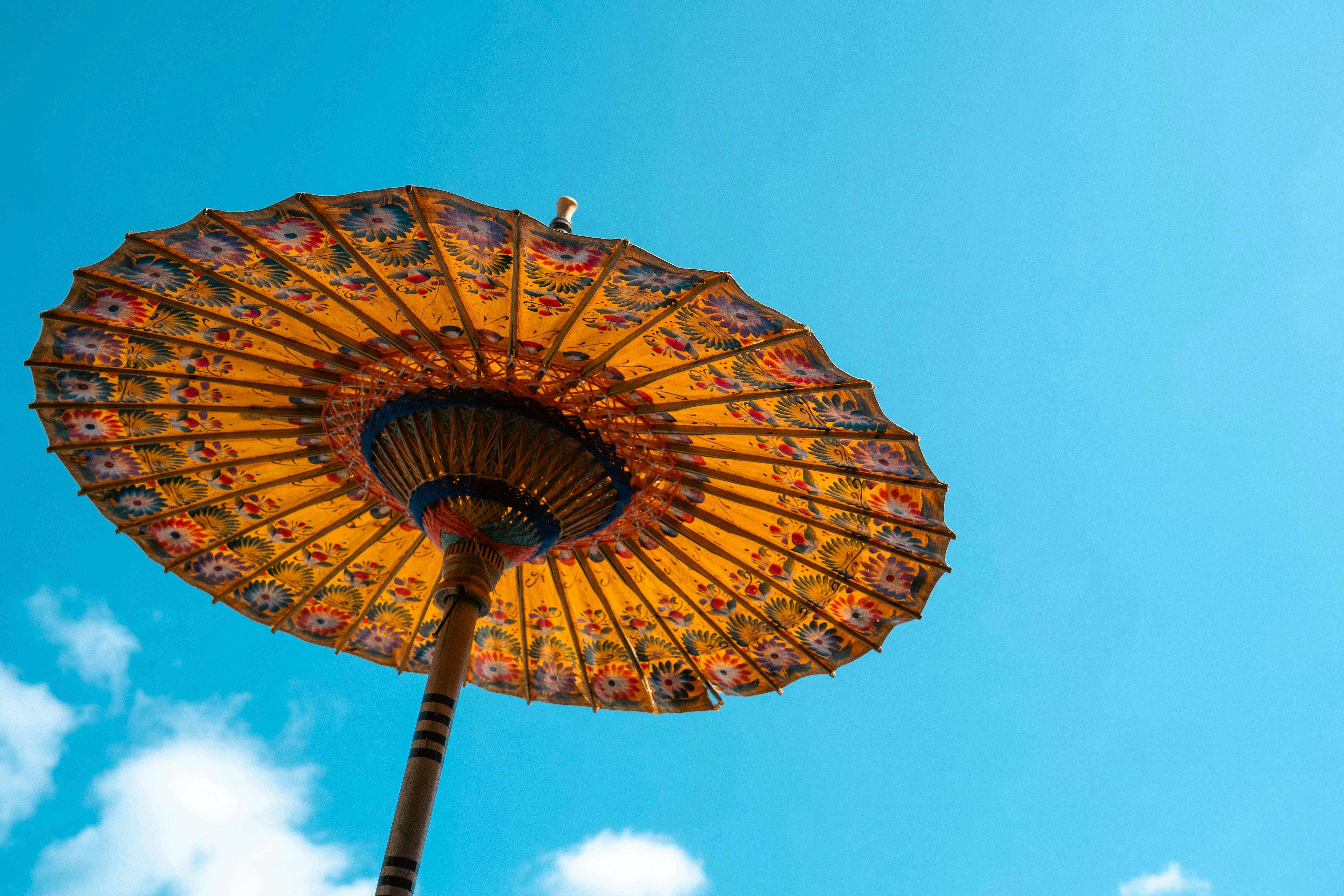 A yellow Balinese umbrella with floral patterns against a bright blue sky