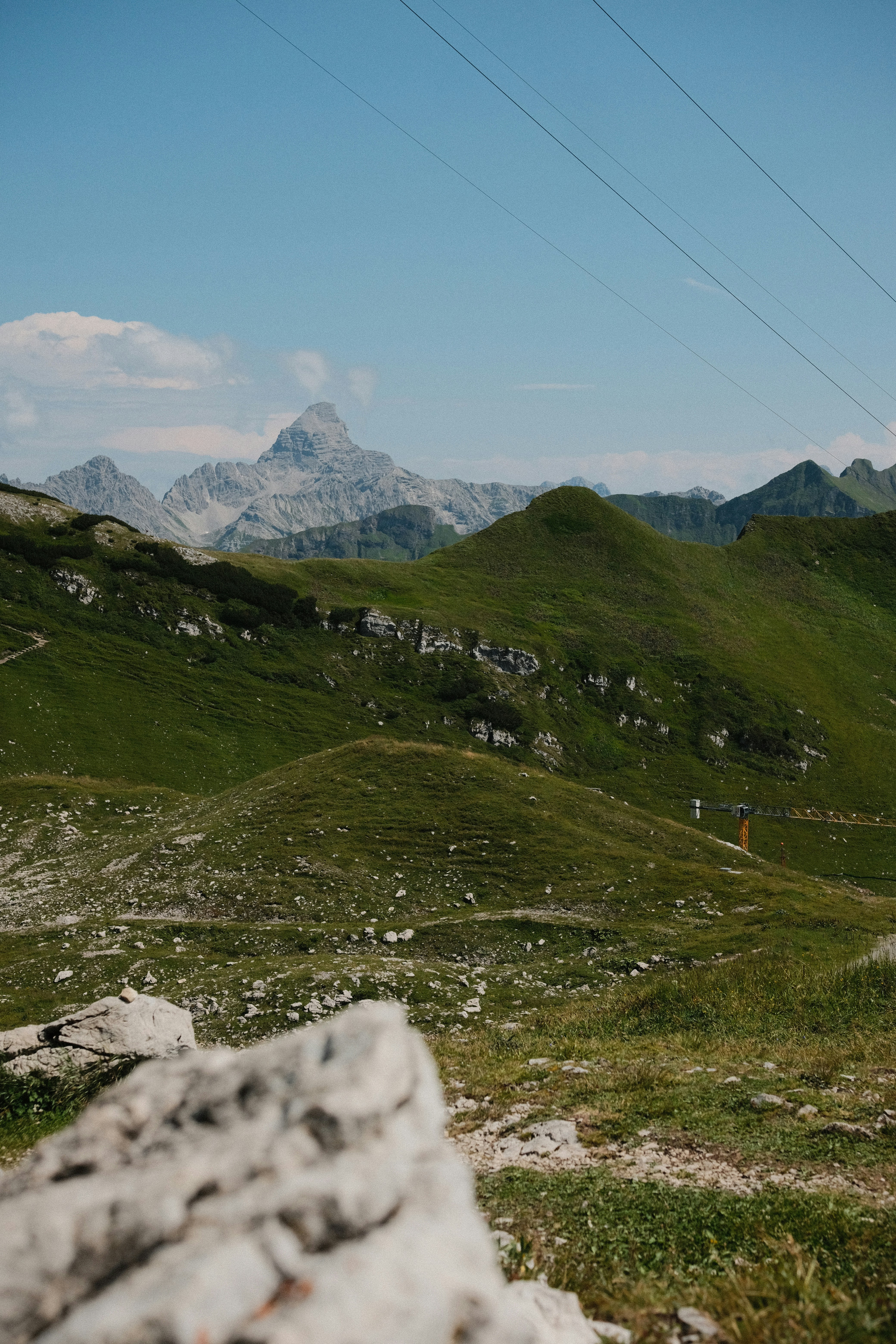 Des pentes verdoyantes de montagne avec des affleurements rocheux et un sommet déchiqueté sous un ciel bleu.