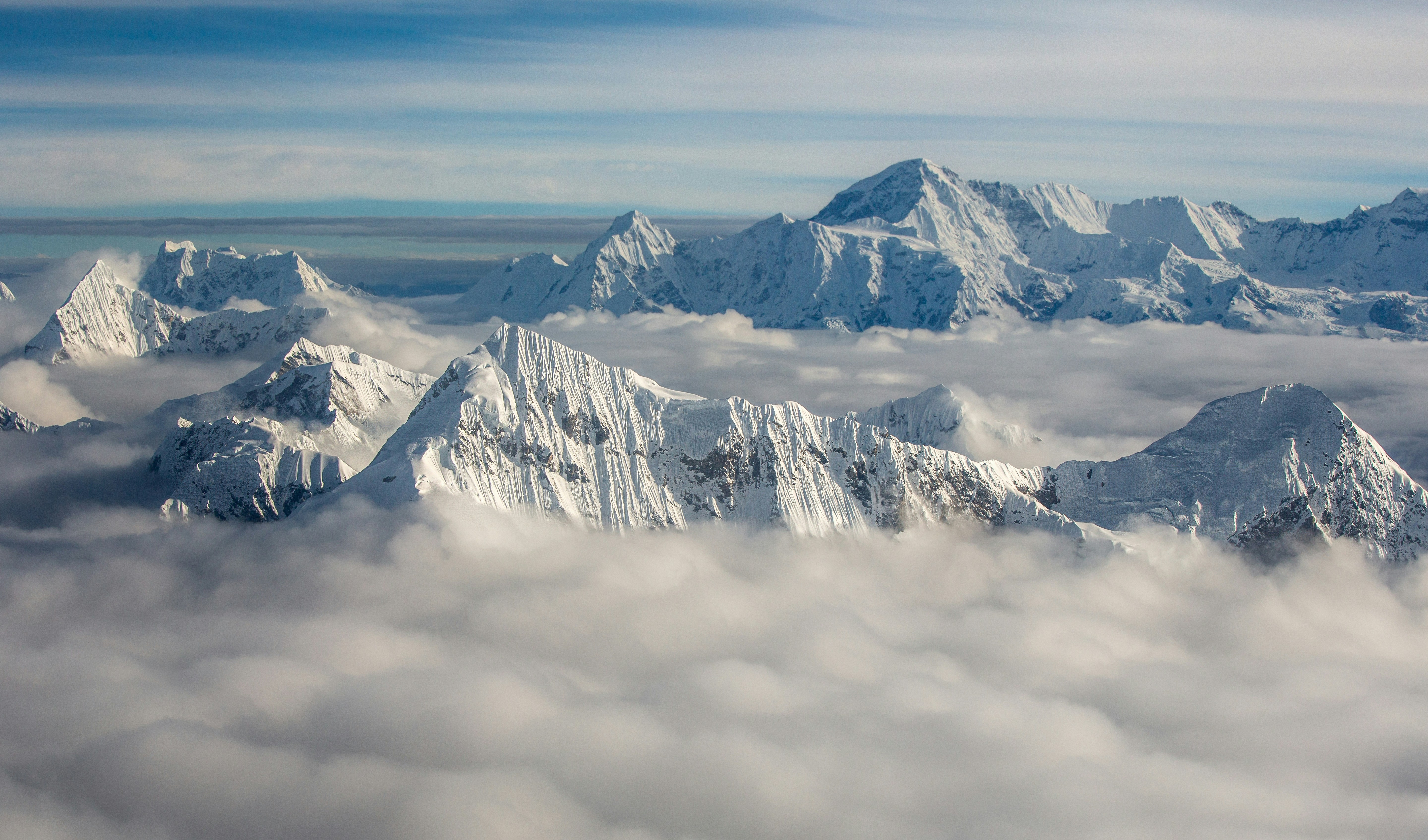 Snow-covered mountain peaks rising above a thick layer of white clouds