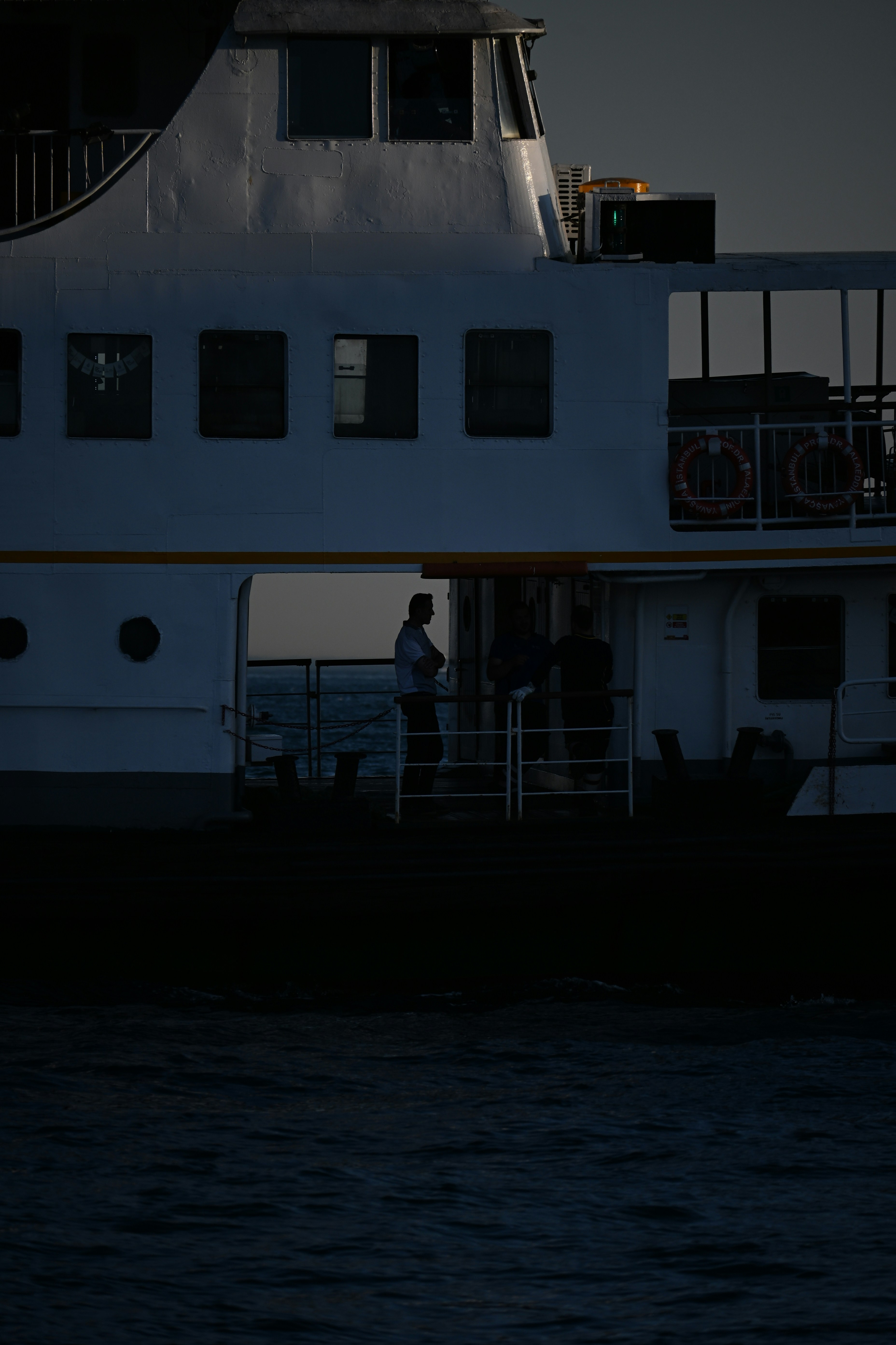 Tres personas en silueta en la cubierta de un ferry en alta mar