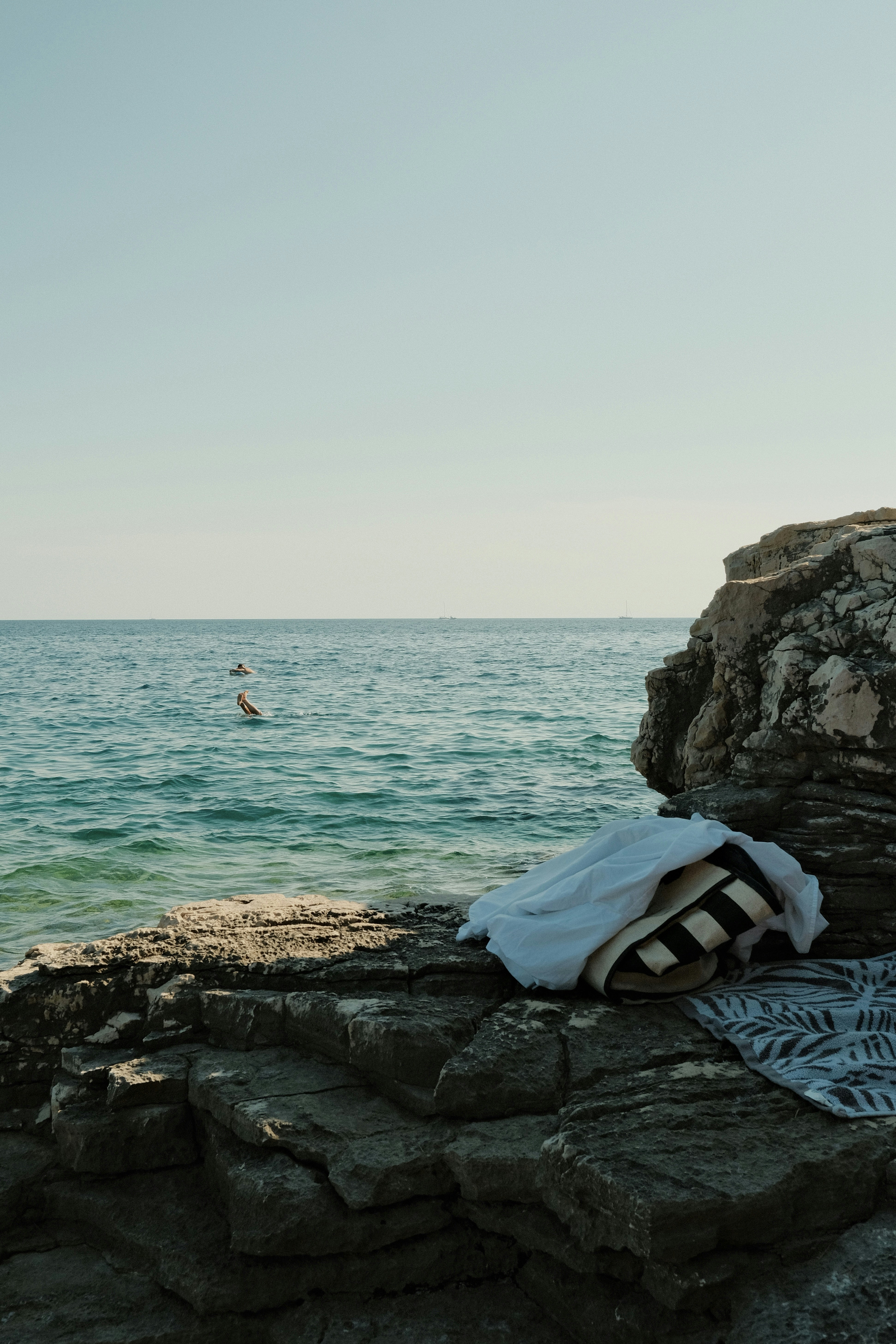 A white shirt and striped bag on rocky cliffs above the blue sea.
