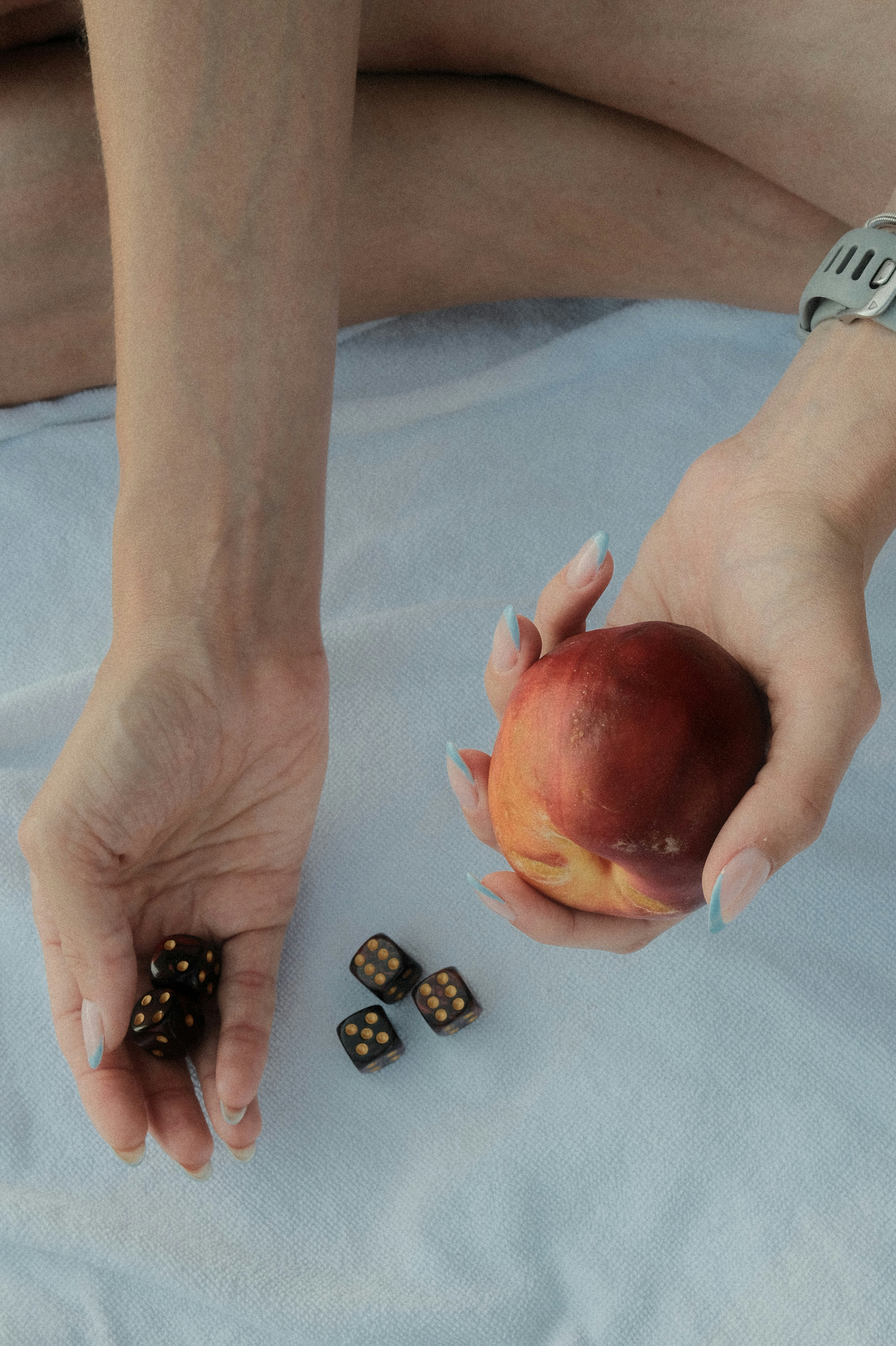 A person holding a peach and black dice on a light blue fabric.