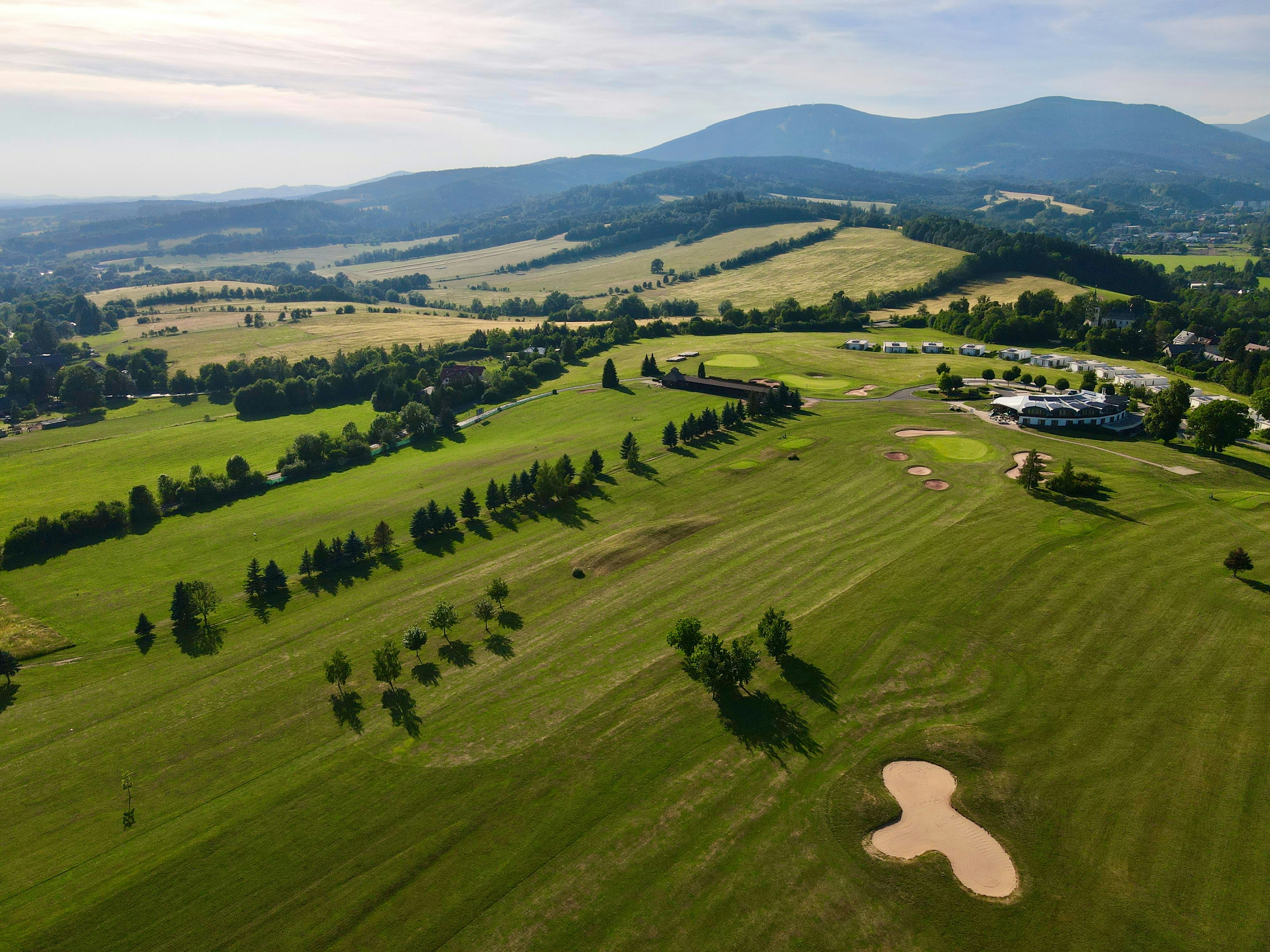 An aerial view of a green golf course with sand bunkers and distant mountains