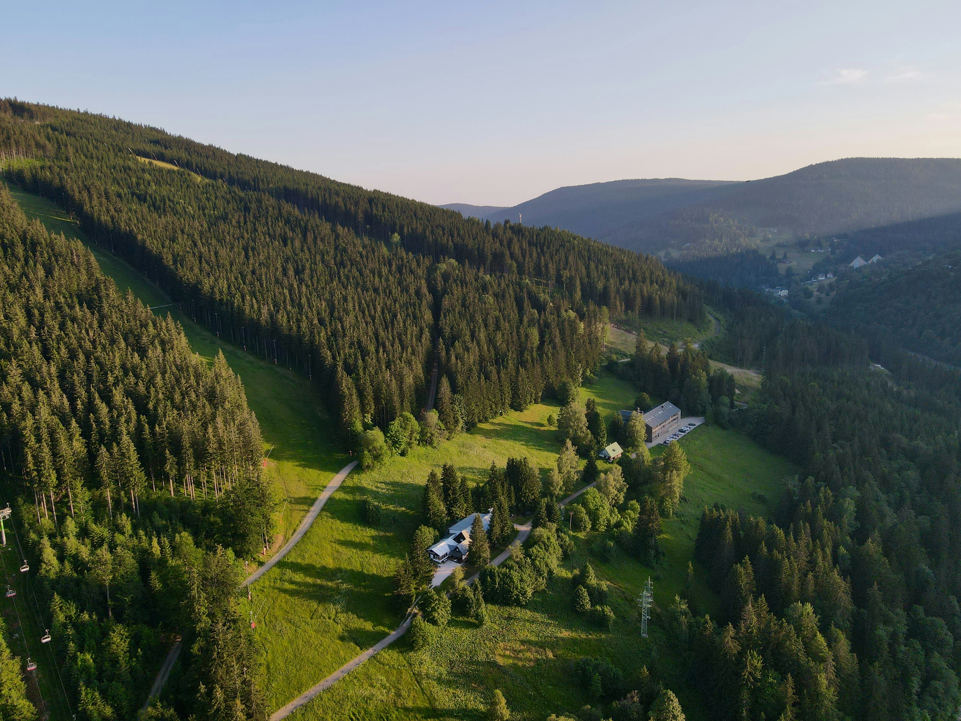 An aerial view of a forested mountain slope with buildings in a green valley