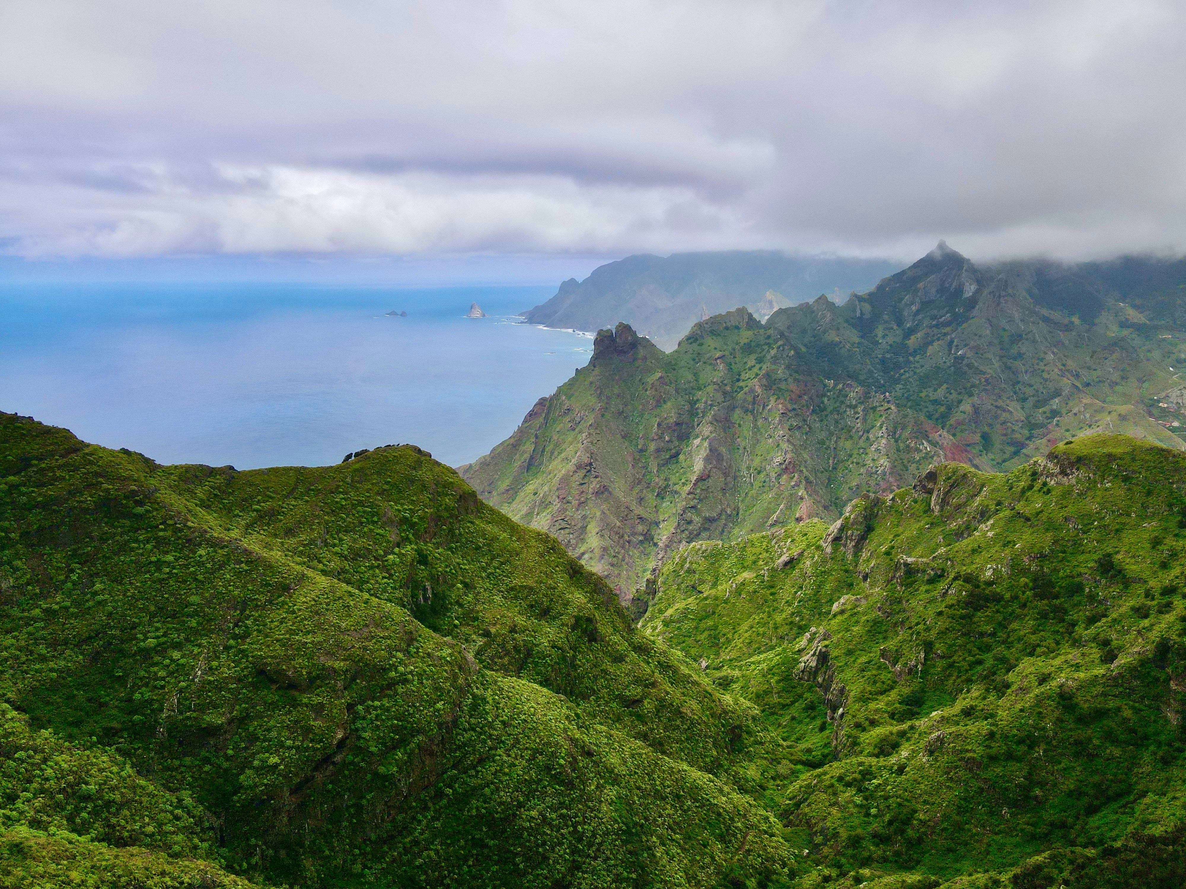 Green mountain ridges sloping down toward the blue ocean under a cloudy sky