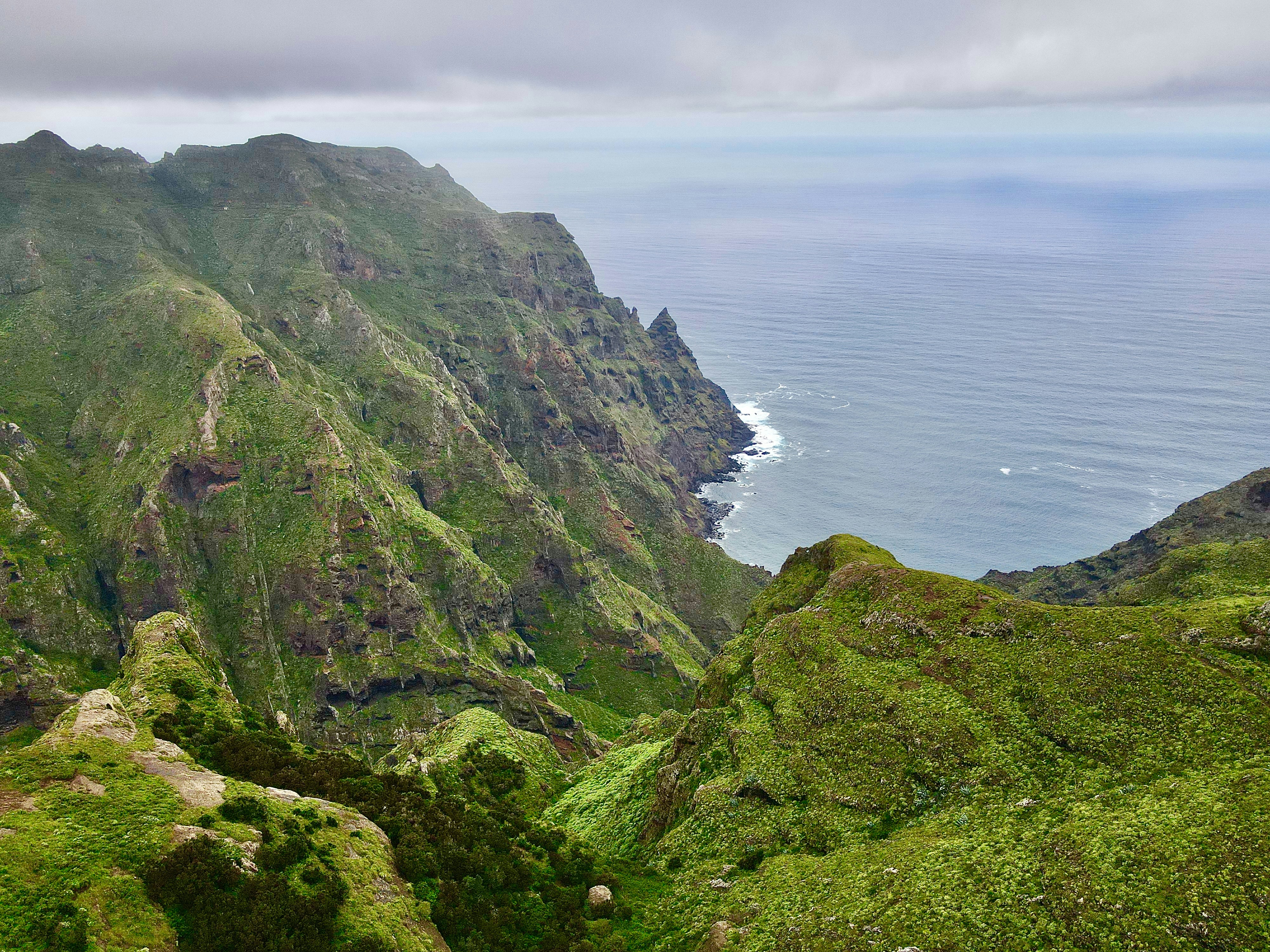 Green mountain ridges sloping down to the ocean under a cloudy sky