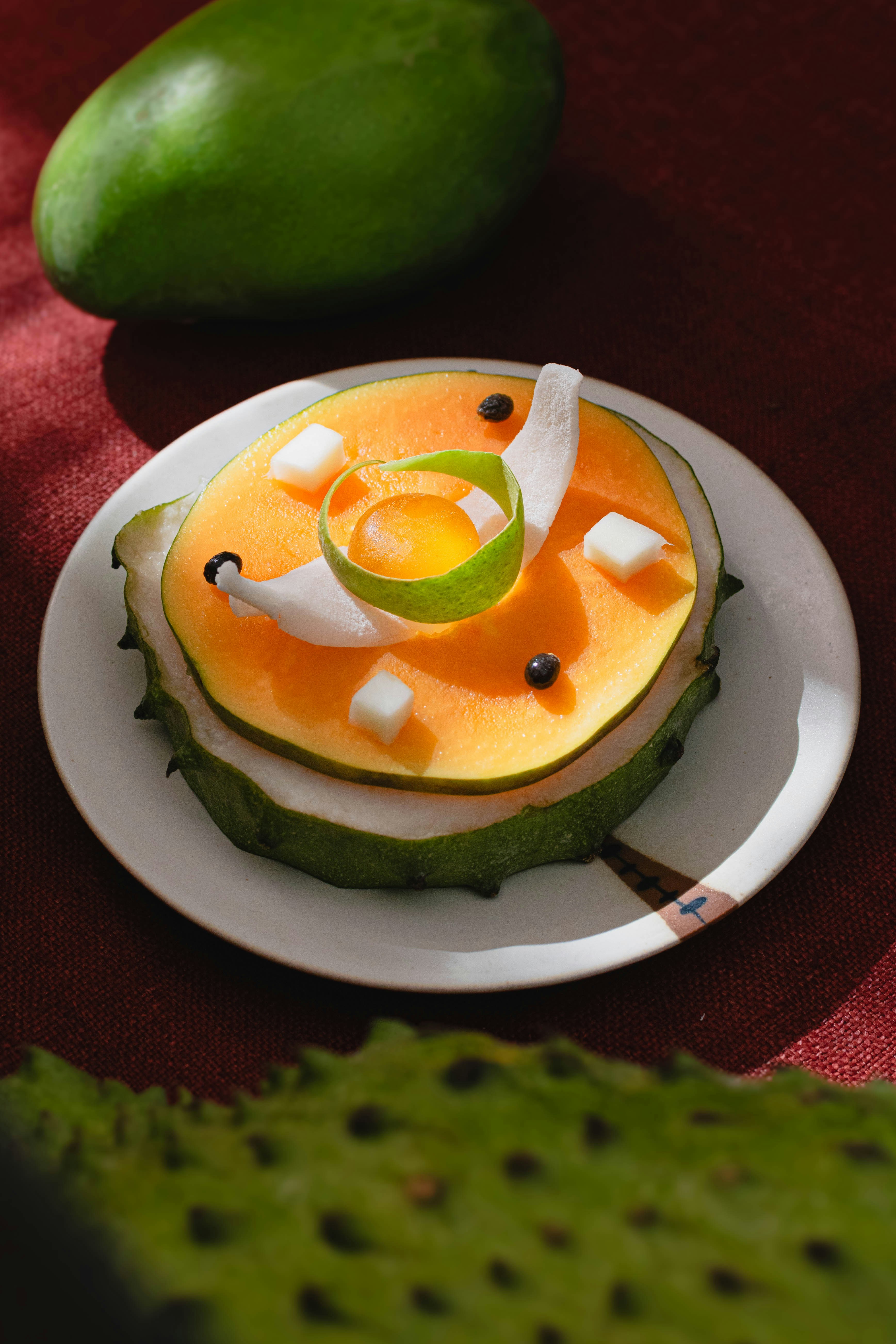 A sliced soursop topped with melon, lime zest, and coconut on a plate