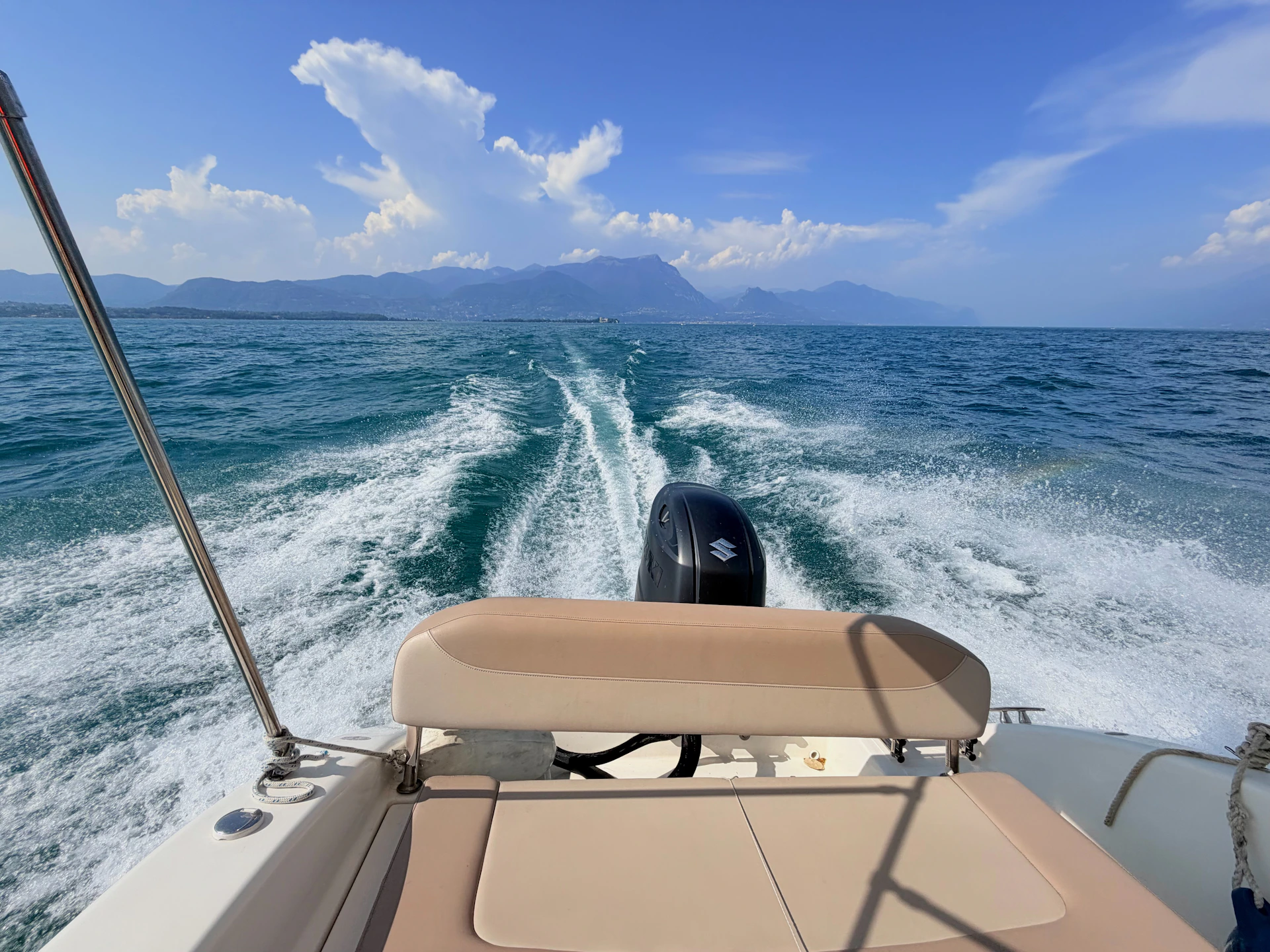 A motorboat wake trailing across blue water toward distant mountains under a clear sky.