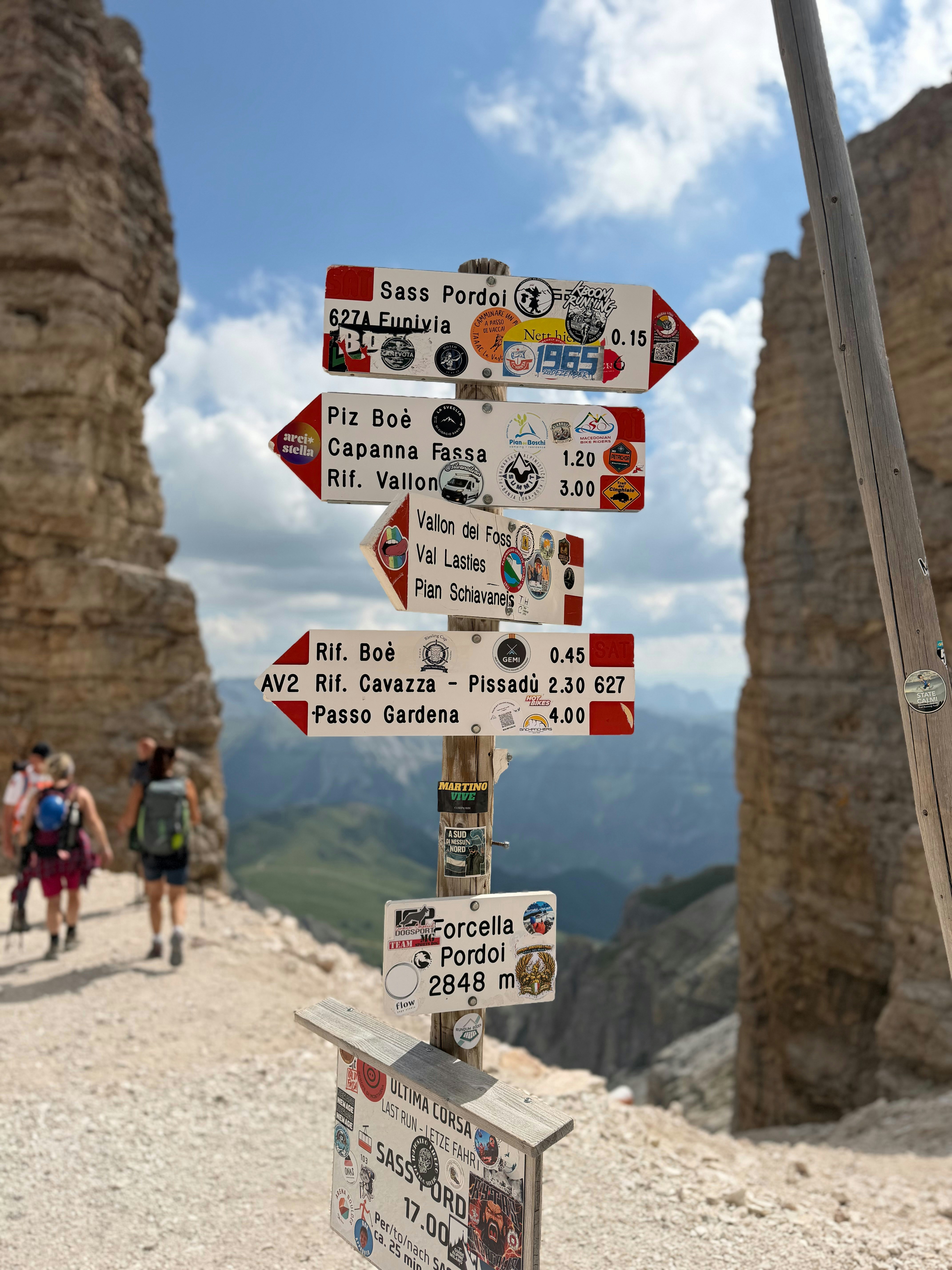 A wooden trail signpost with multiple directional arrows on a mountain pass in the Dolomites