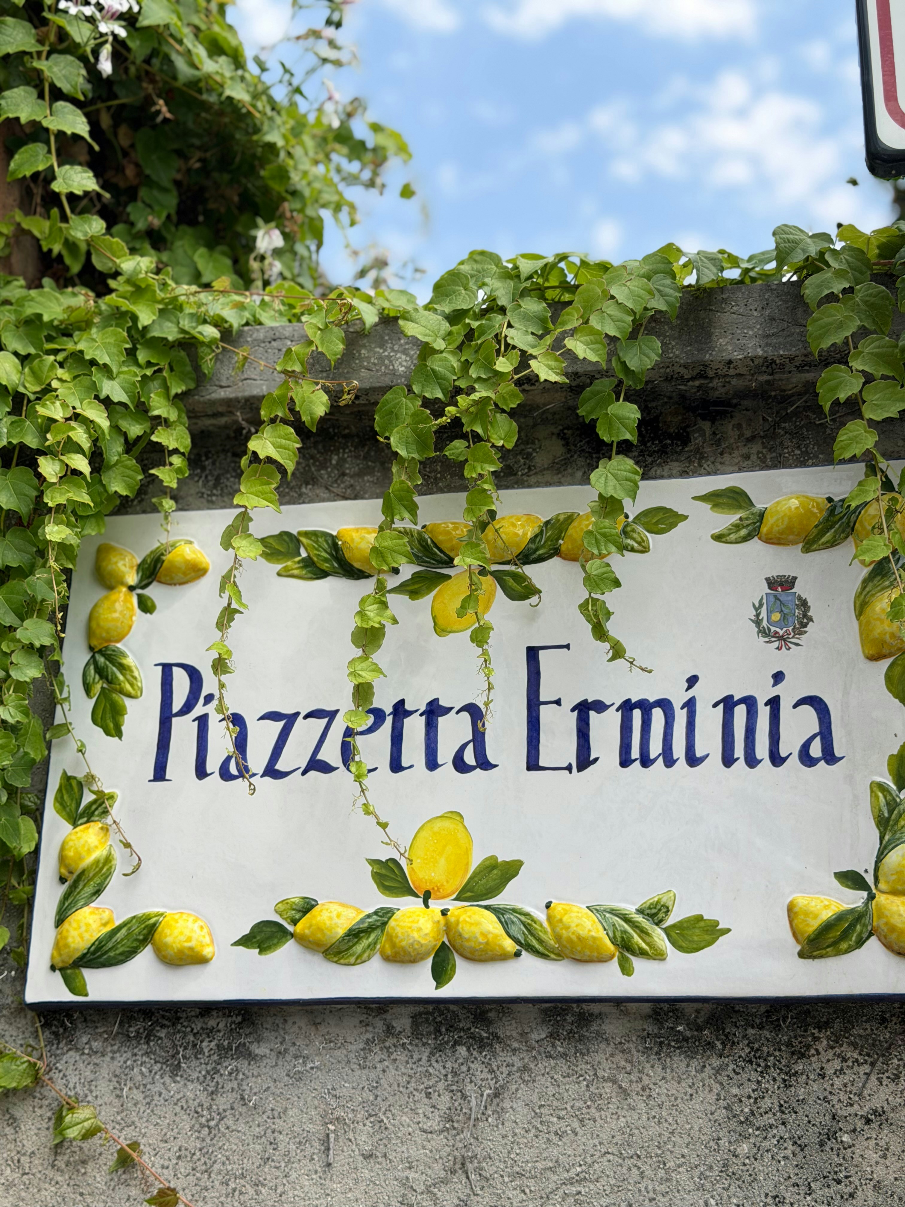 A ceramic sign reading "Piazzetta Erminia" decorated with painted lemons and green vines