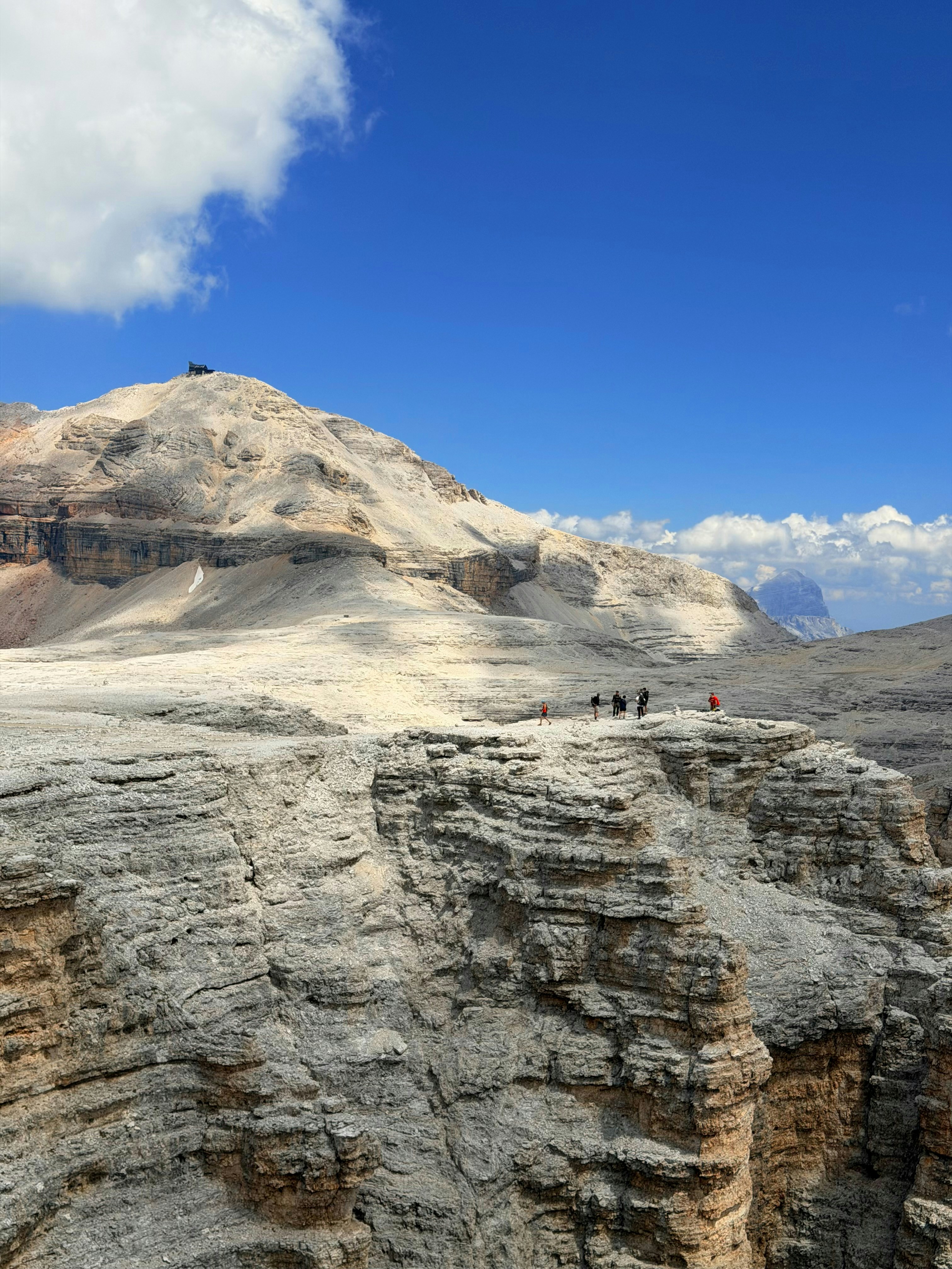A group of hikers on a rocky cliff edge below a mountain peak