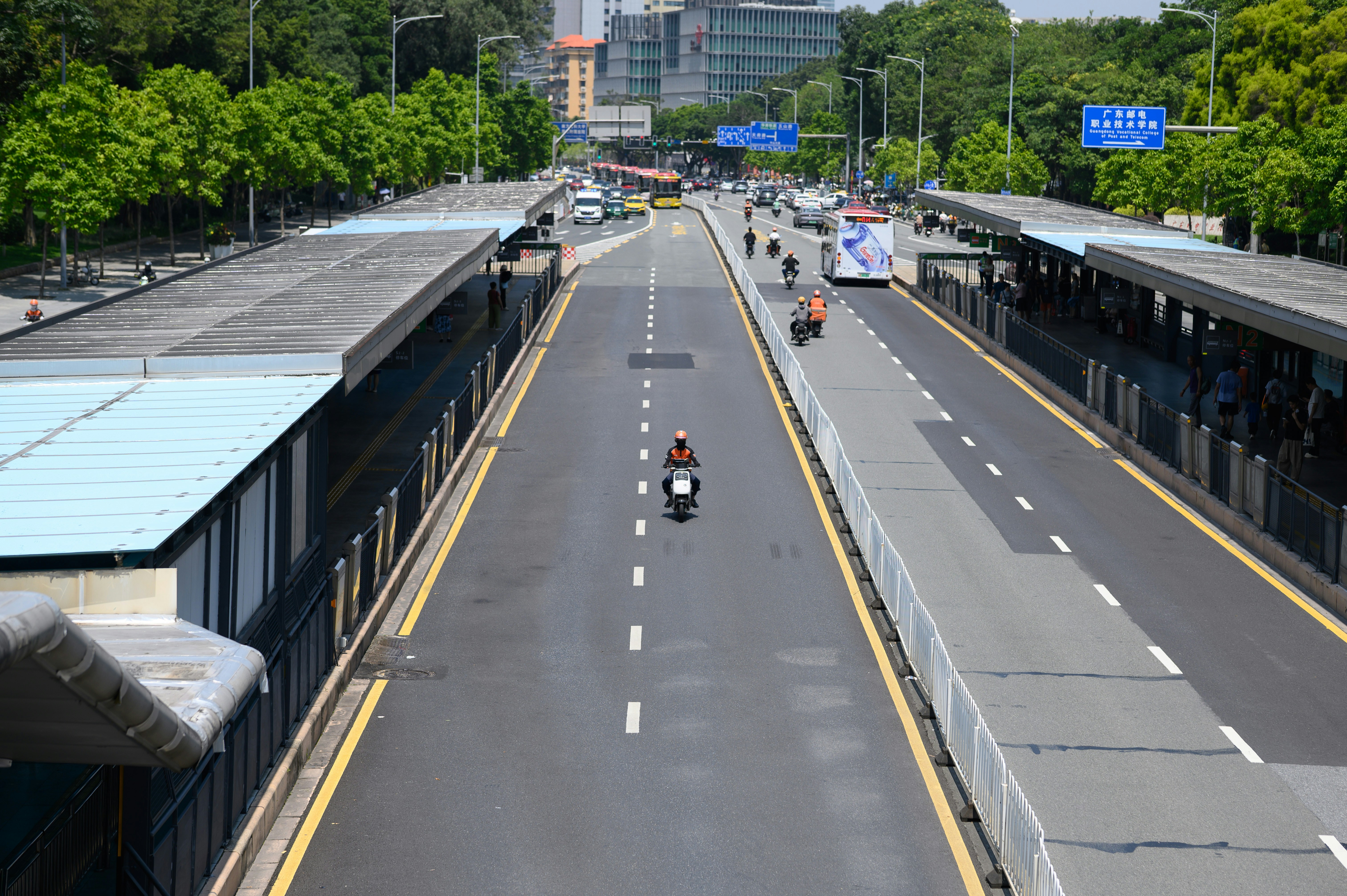 A person riding a scooter on a multi-lane road between two bus stations
