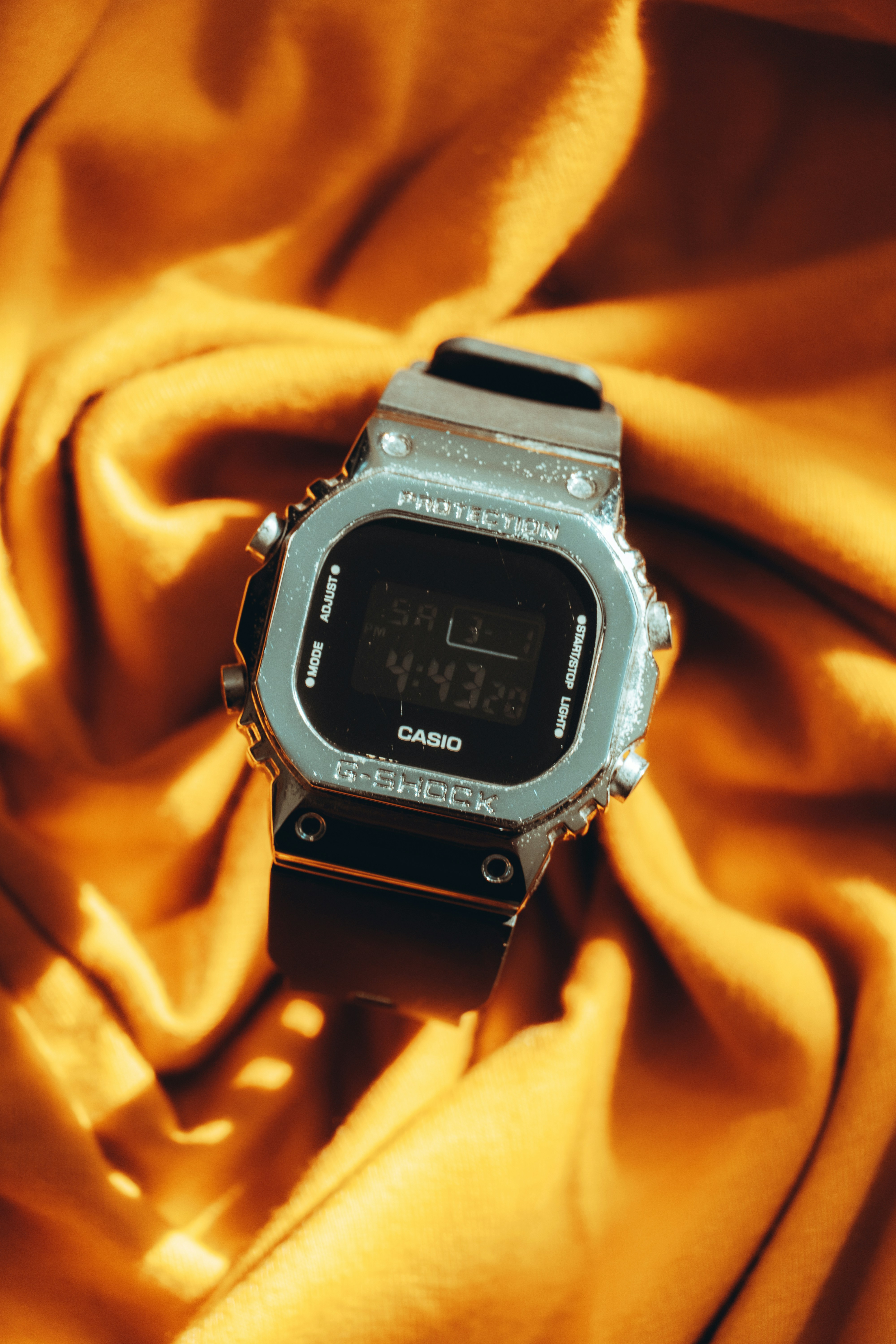A digital watch with a metallic bezel on a draped yellow fabric