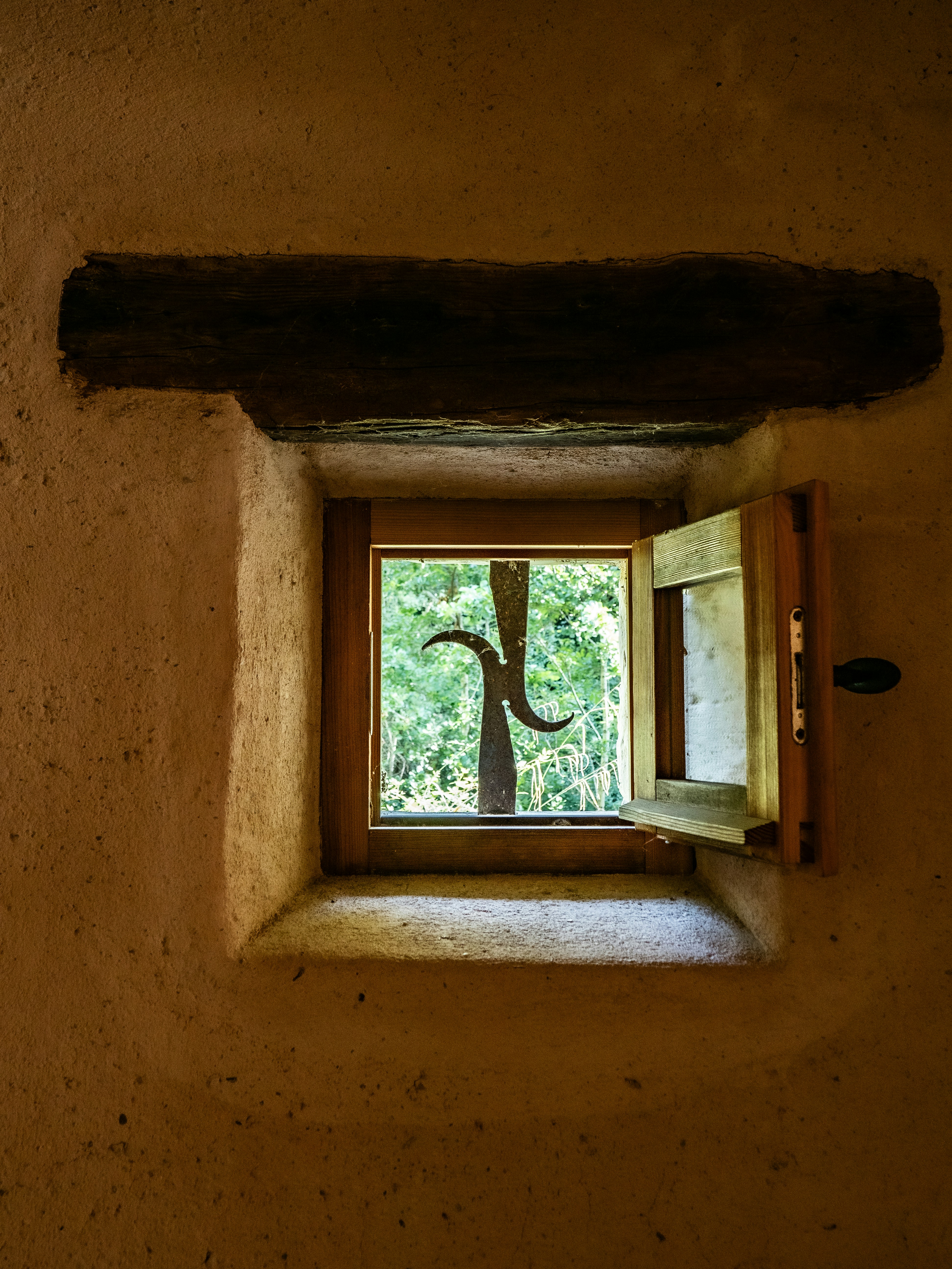 An open wooden window with a metal grille looking out onto green trees