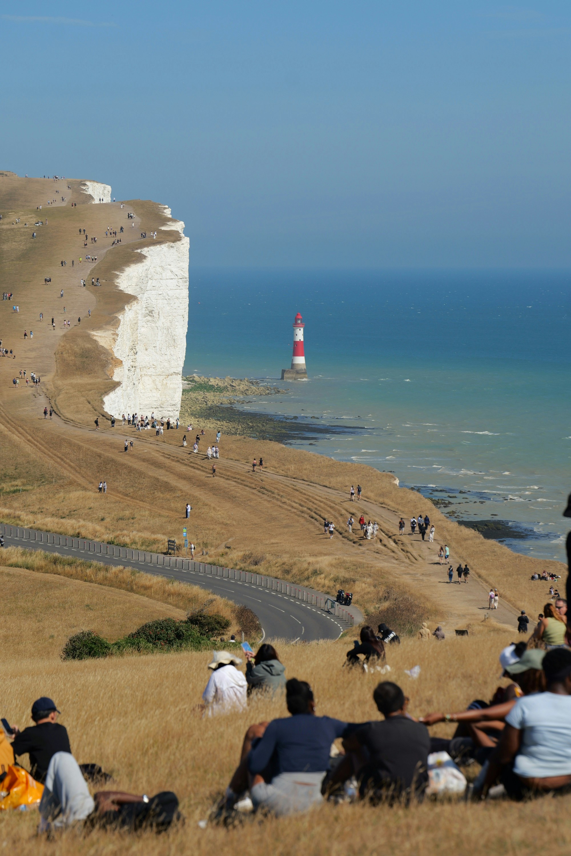 People walking along white chalk cliffs near Beachy Head lighthouse in East Sussex