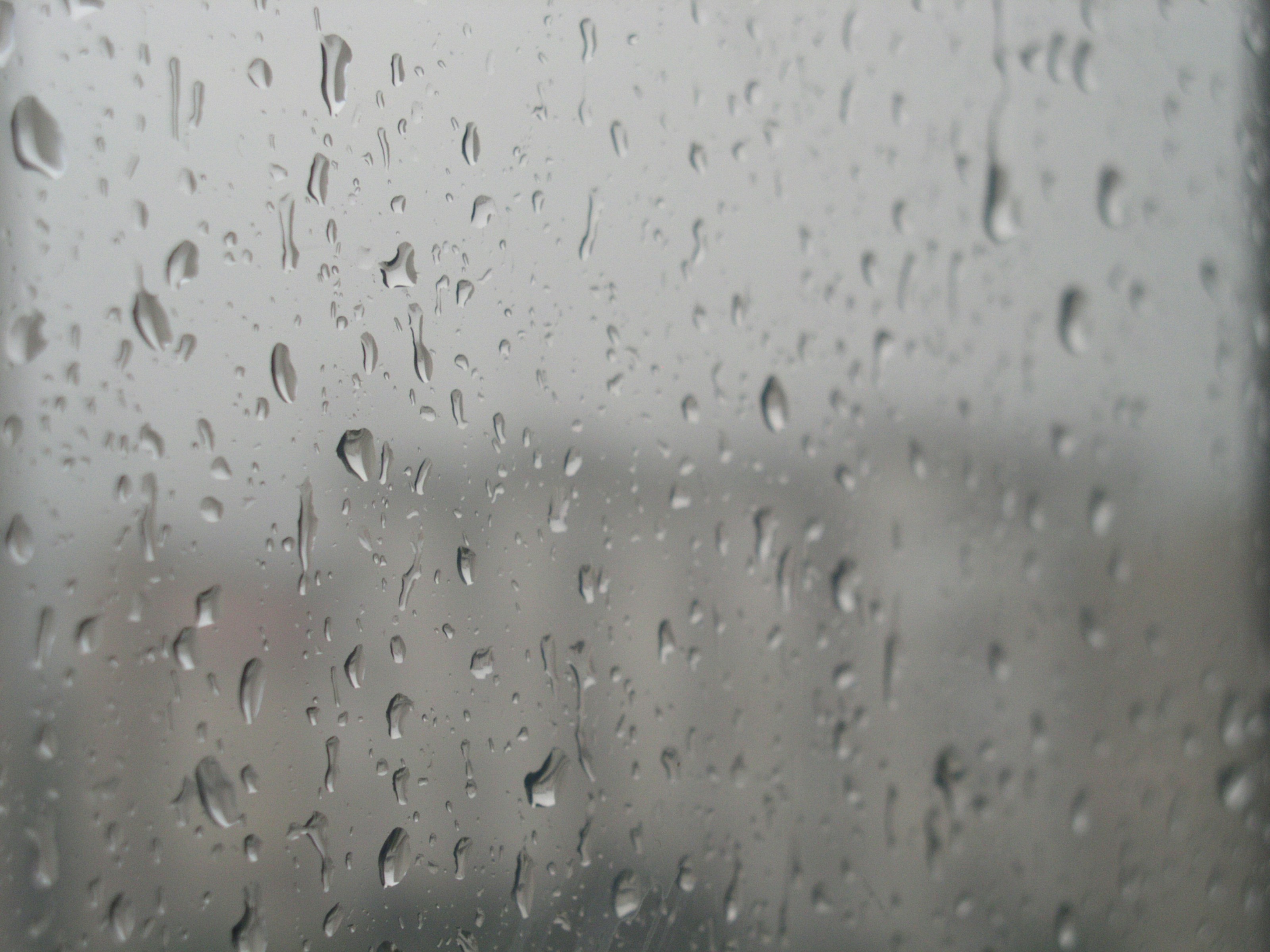 ぼやけた灰色の背景を持つガラス窓に落ちる雨粒。