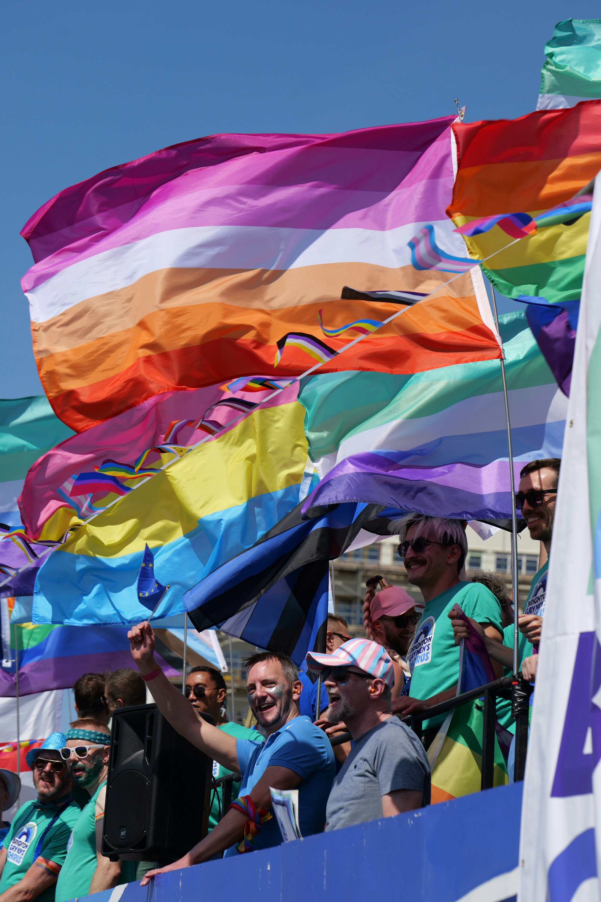 People waving pride flags on a float during a sunny outdoor parade