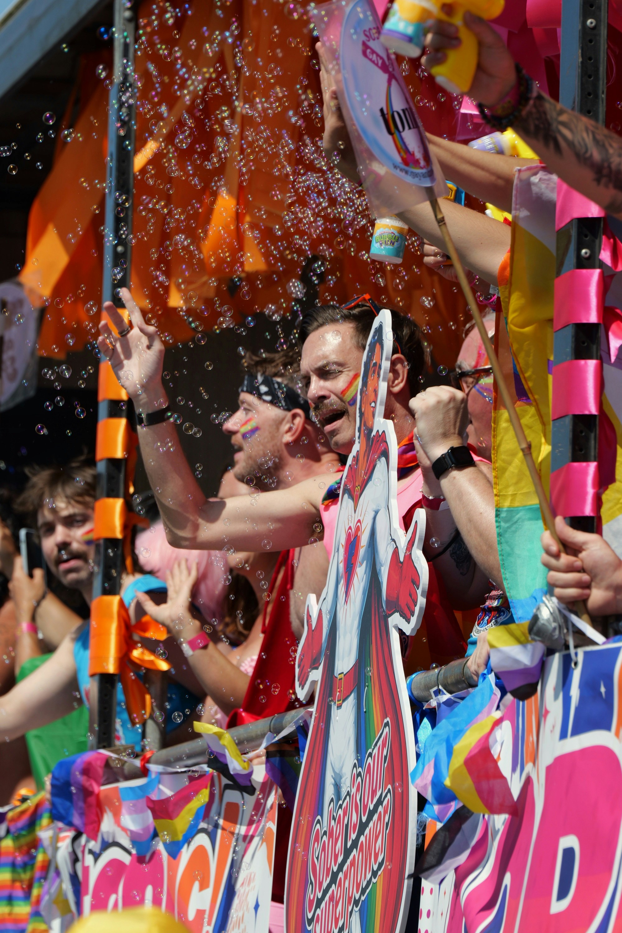 People on a parade float surrounded by bubbles, waving and celebrating at a pride event