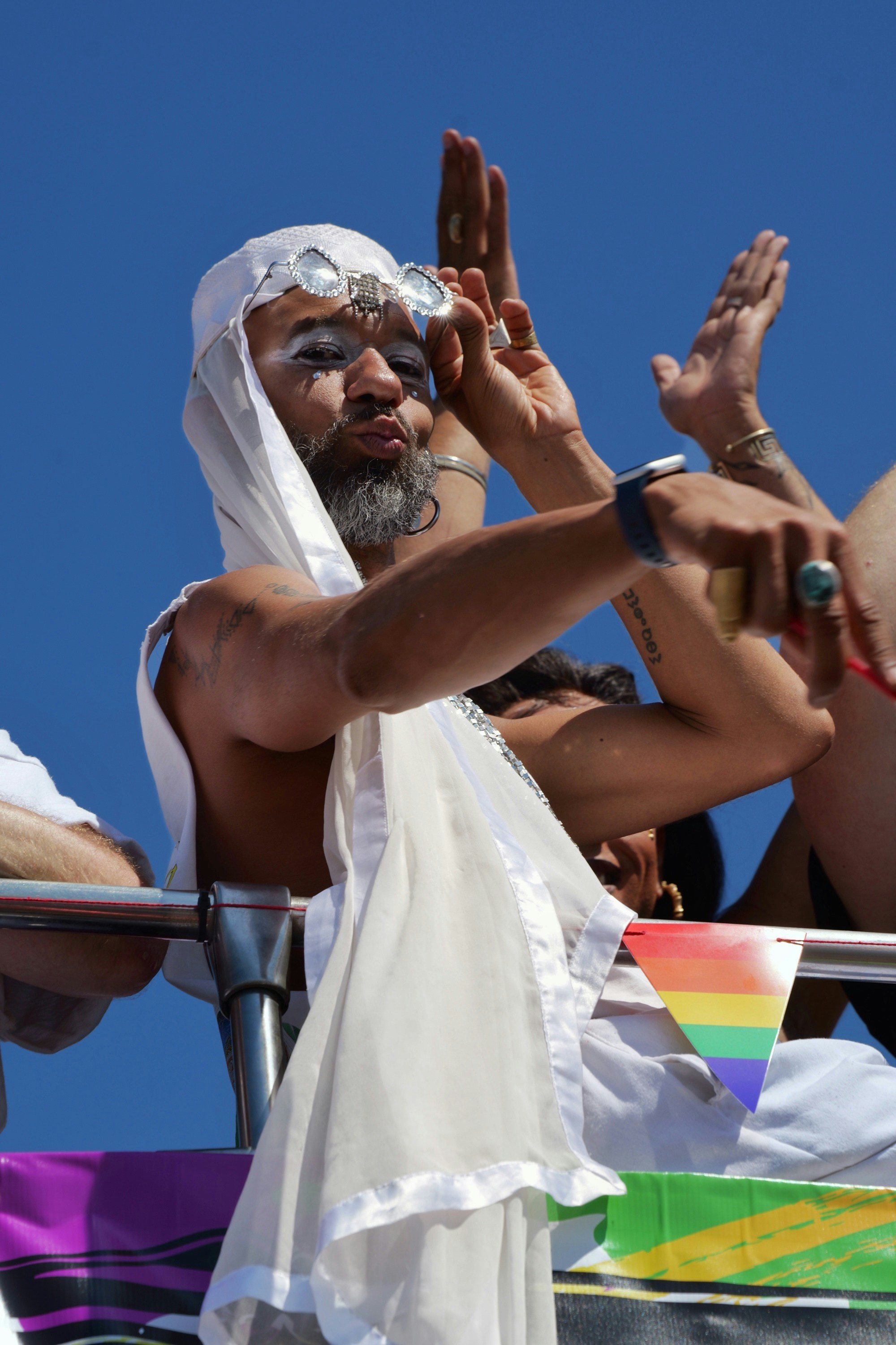 A person in a white headscarf and glittery glasses waving from a parade float