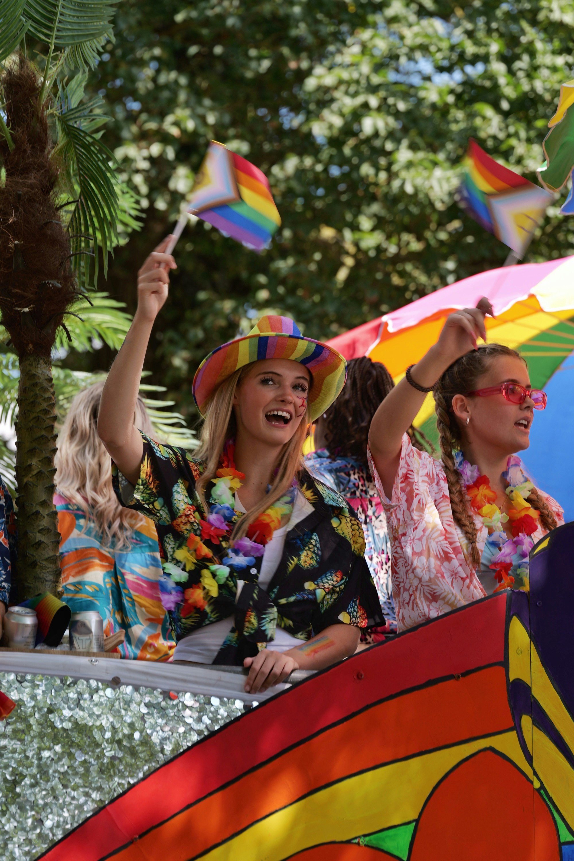 Two women waving pride flags on a colorful parade float outdoors