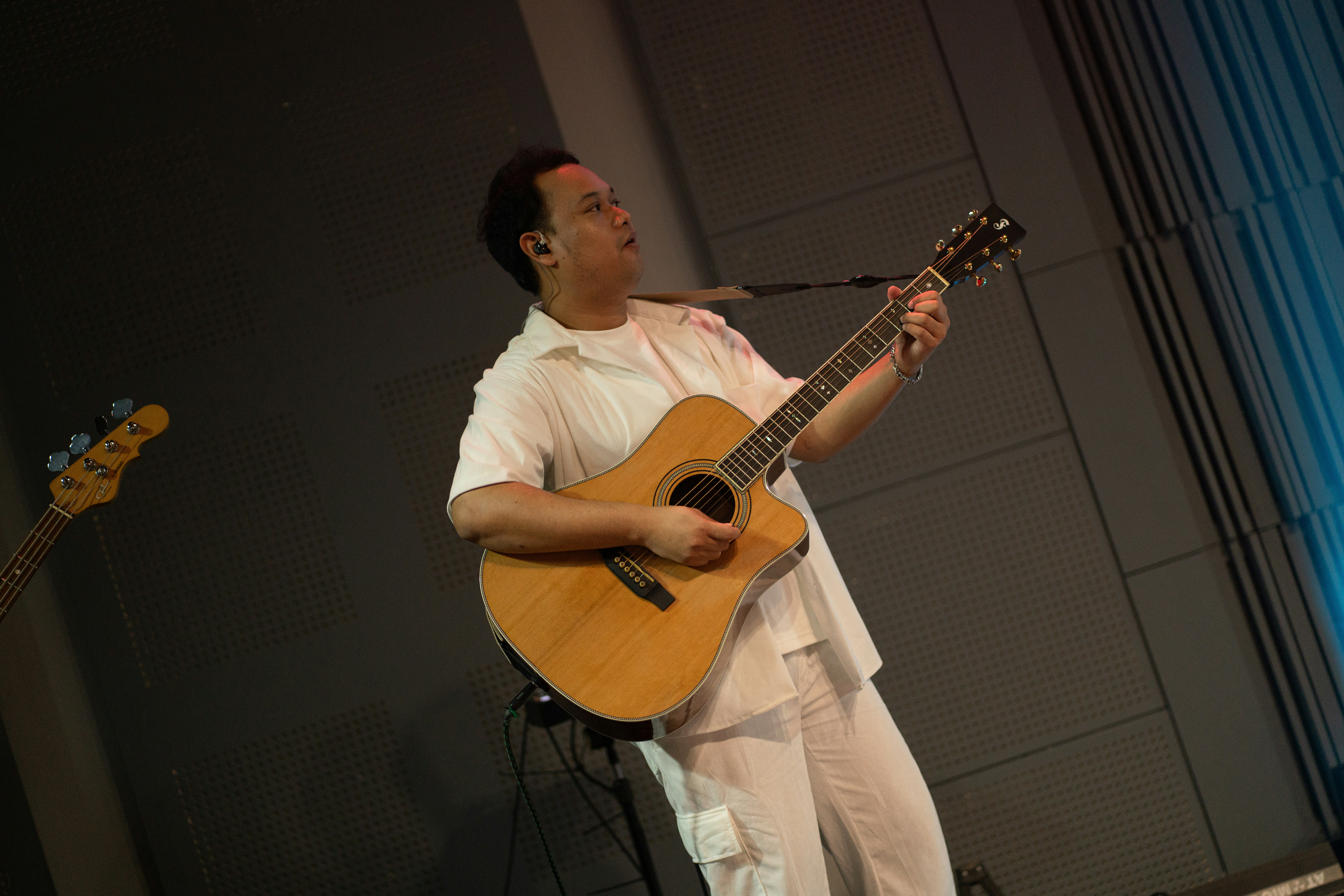 Un hombre con camisa blanca tocando la guitarra acústica en un escenario