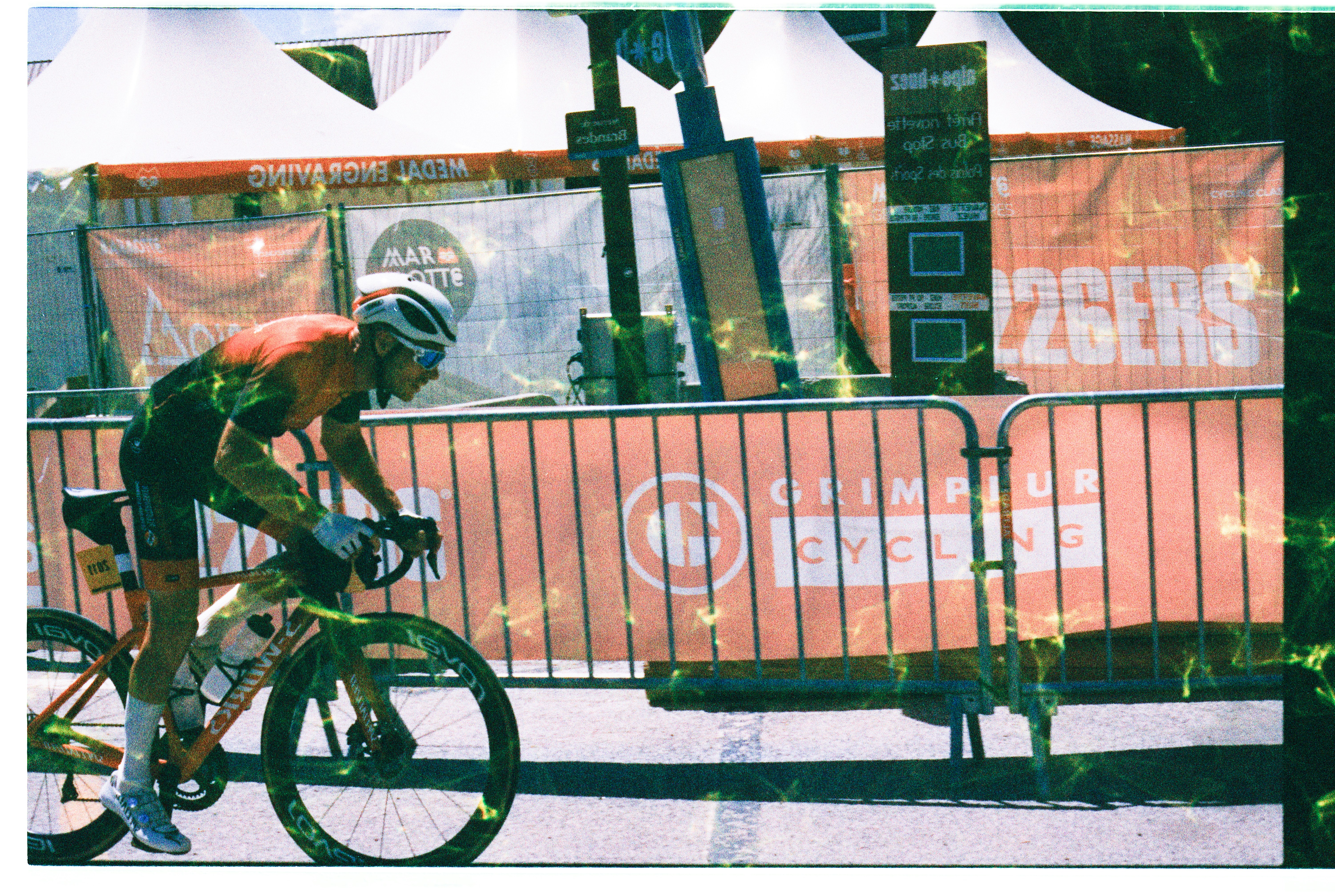A cyclist in a red and black jersey riding past orange event barriers