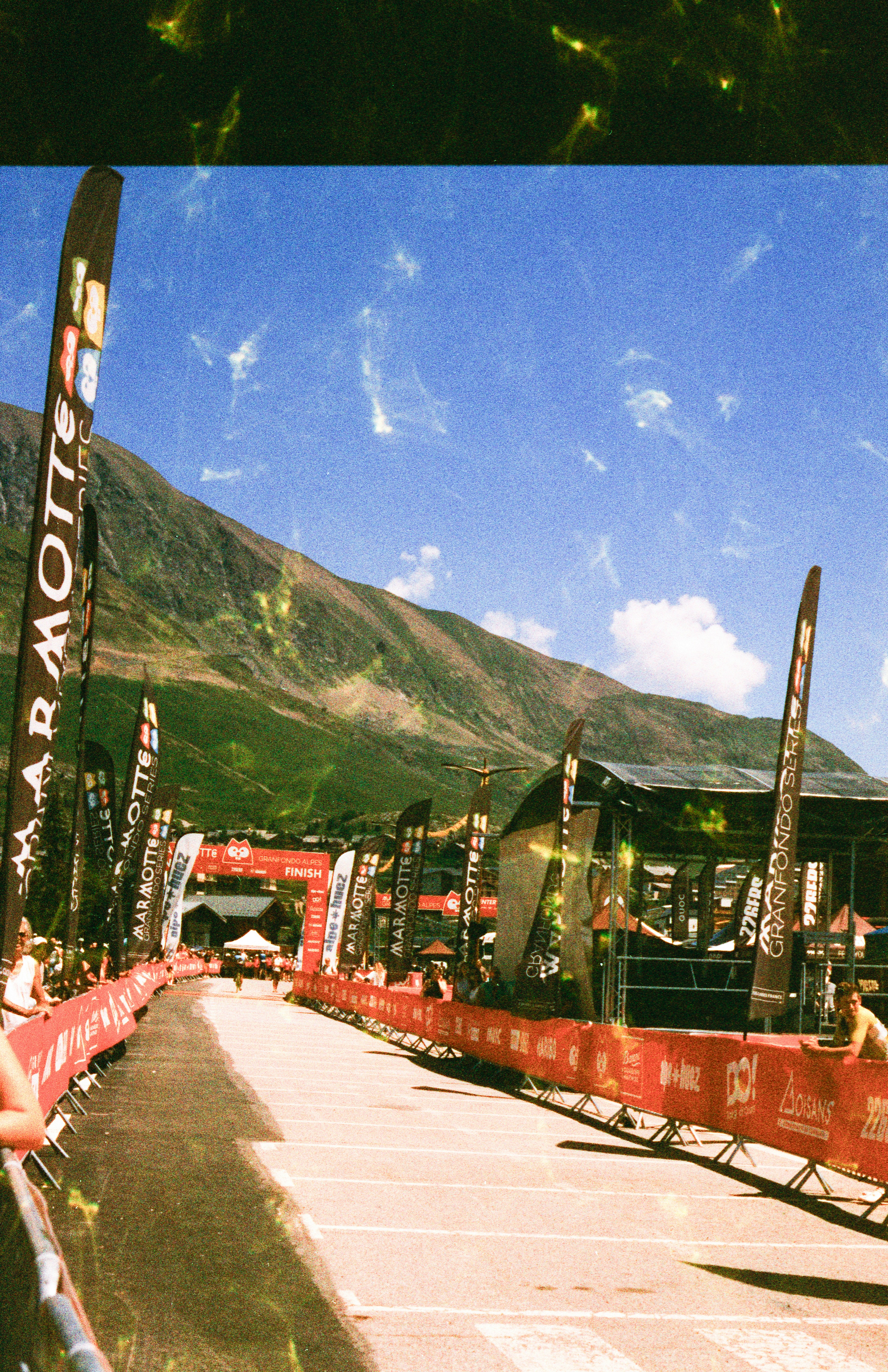 A cycling race finish line with red banners and flags under a mountain