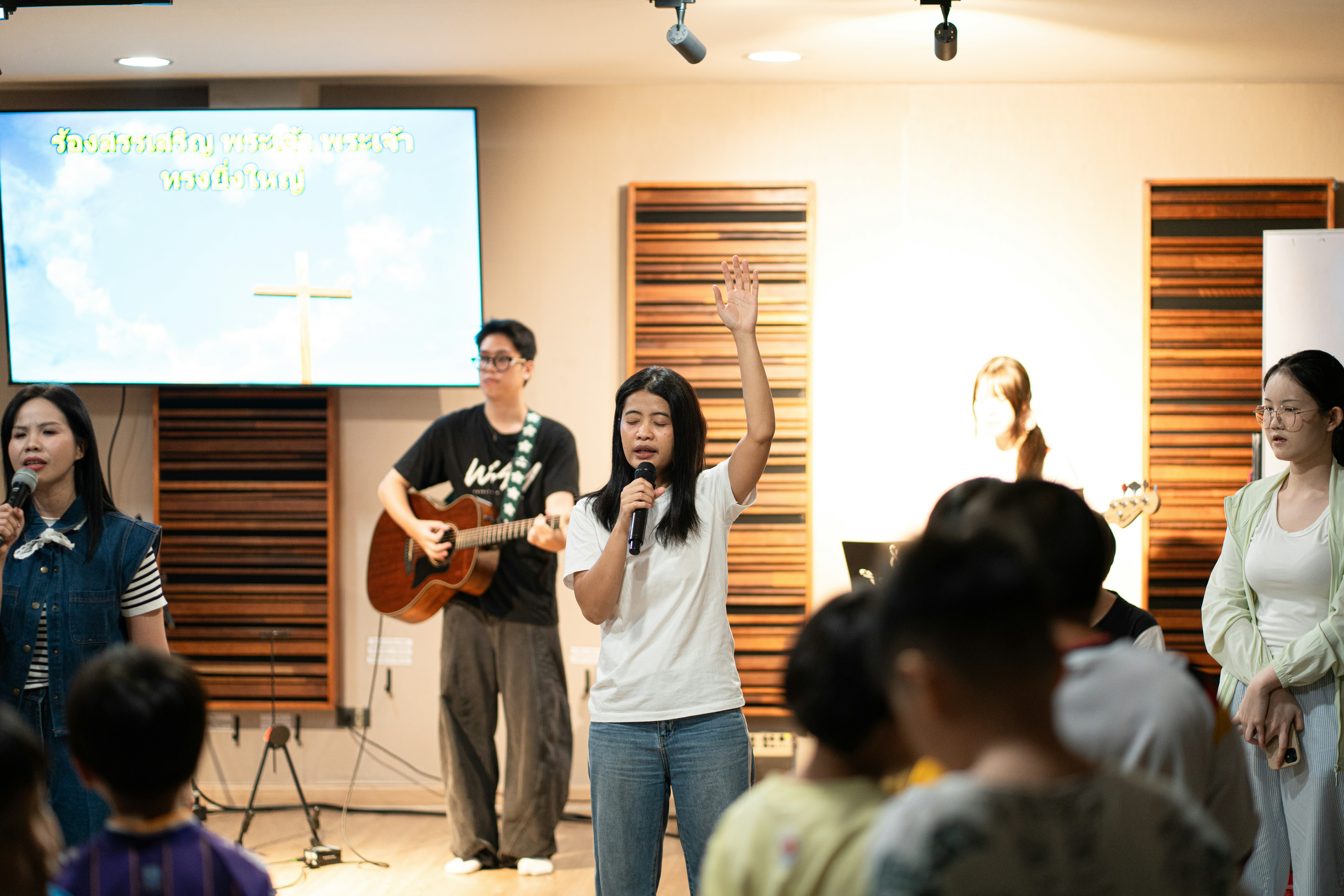 A woman singing with a microphone and raised hand in a church worship service.