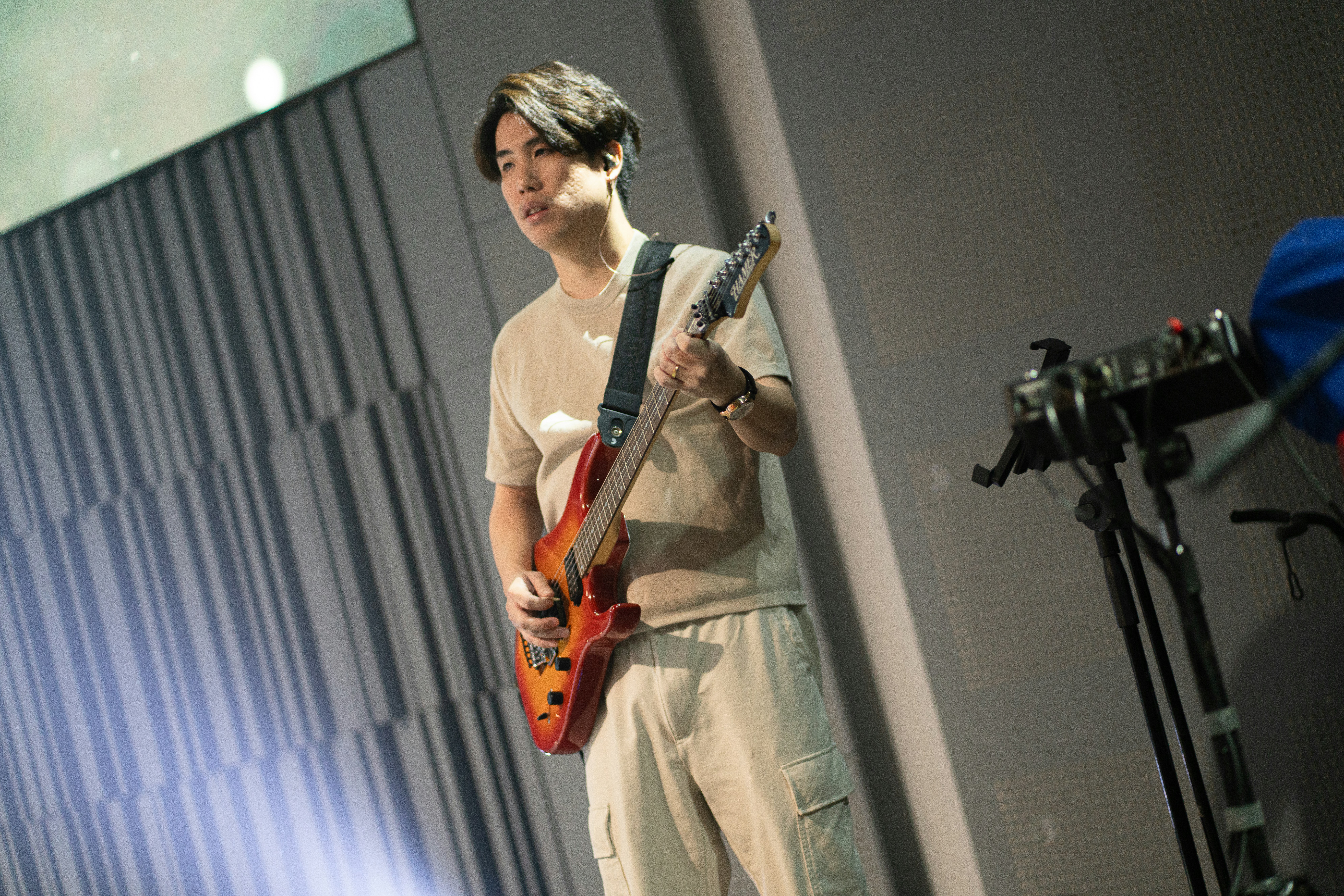 A person playing a red electric guitar in a room with grey walls.