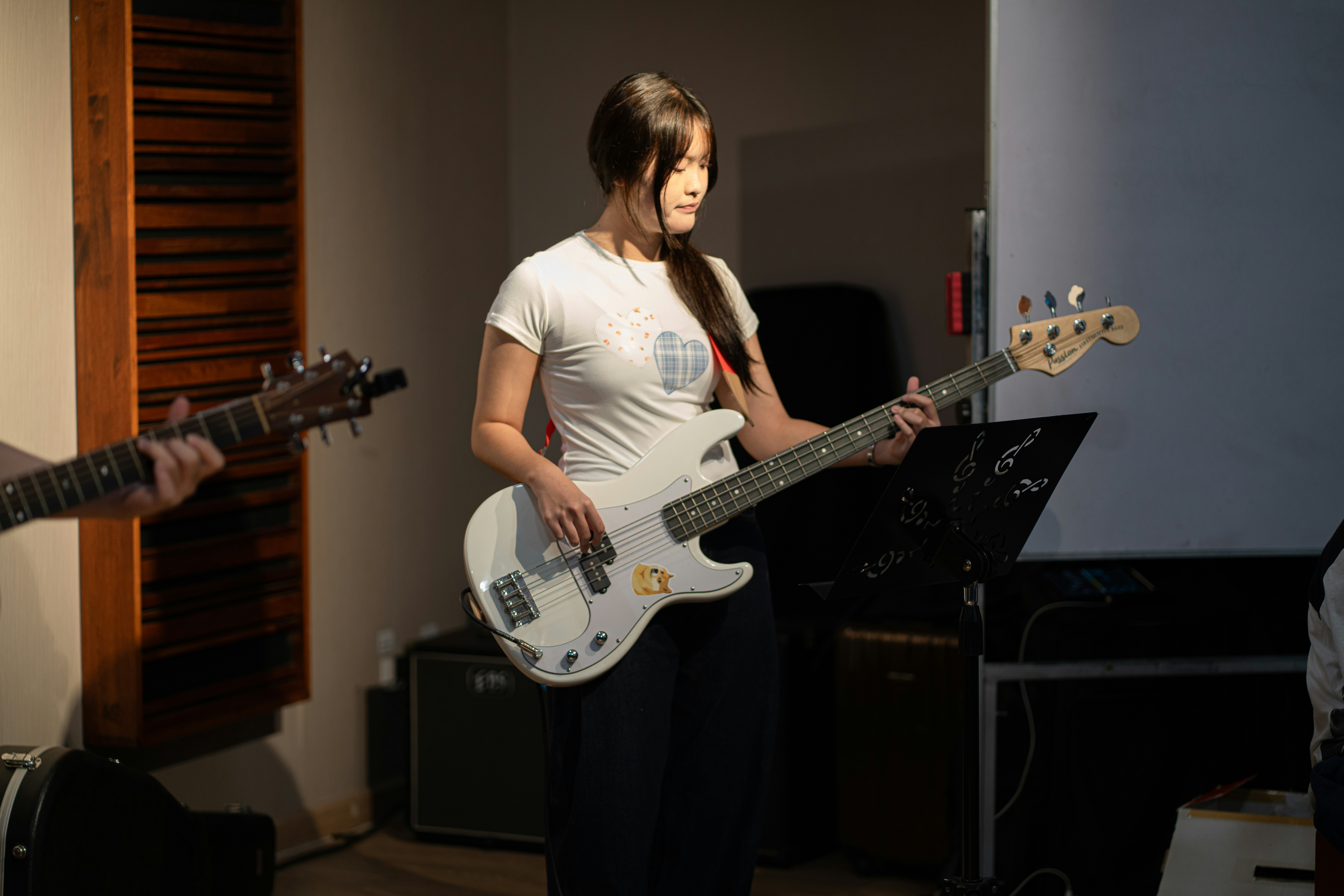 A woman playing a white bass guitar in a music rehearsal room.