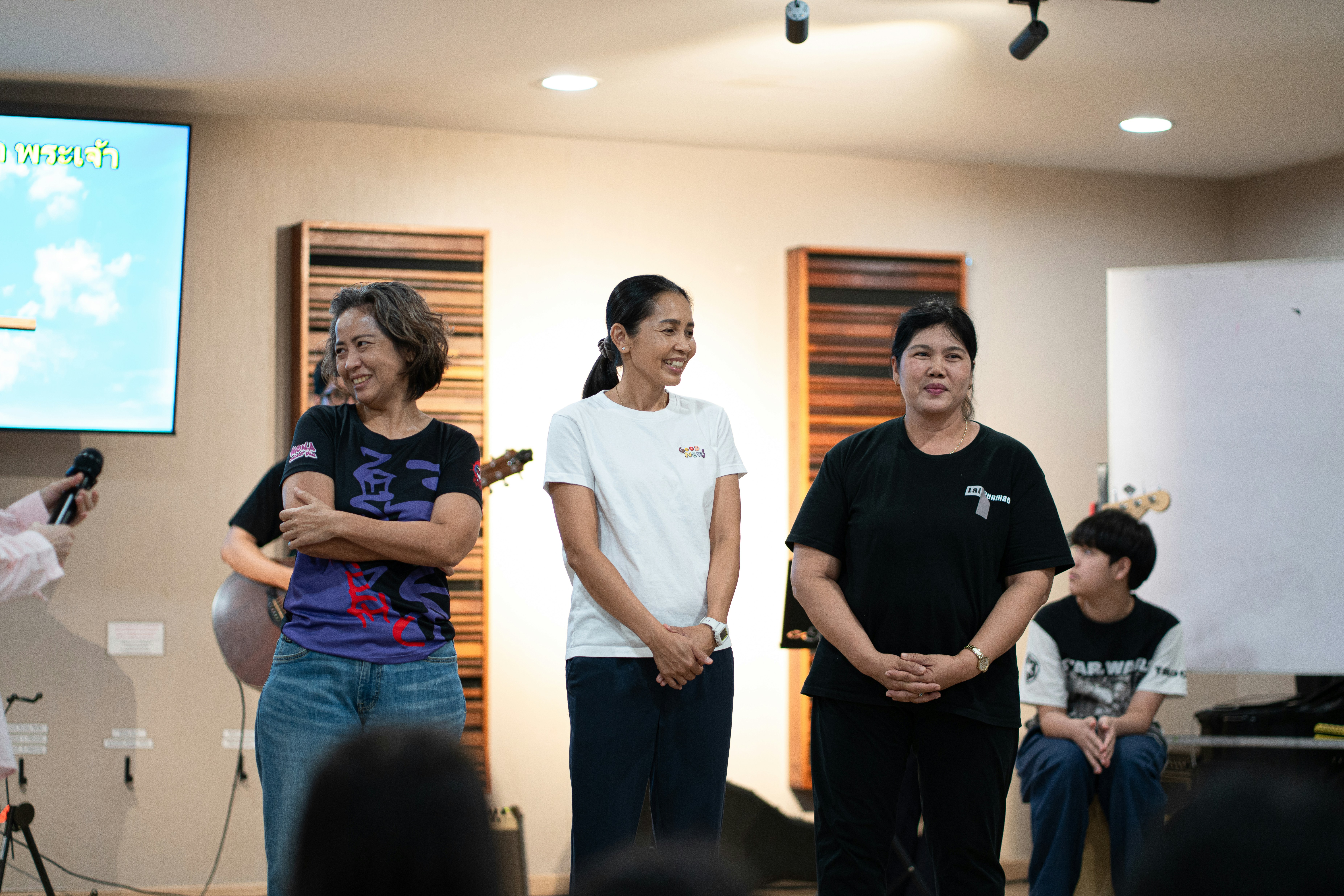 Three women standing in a row in a room with acoustic panels.