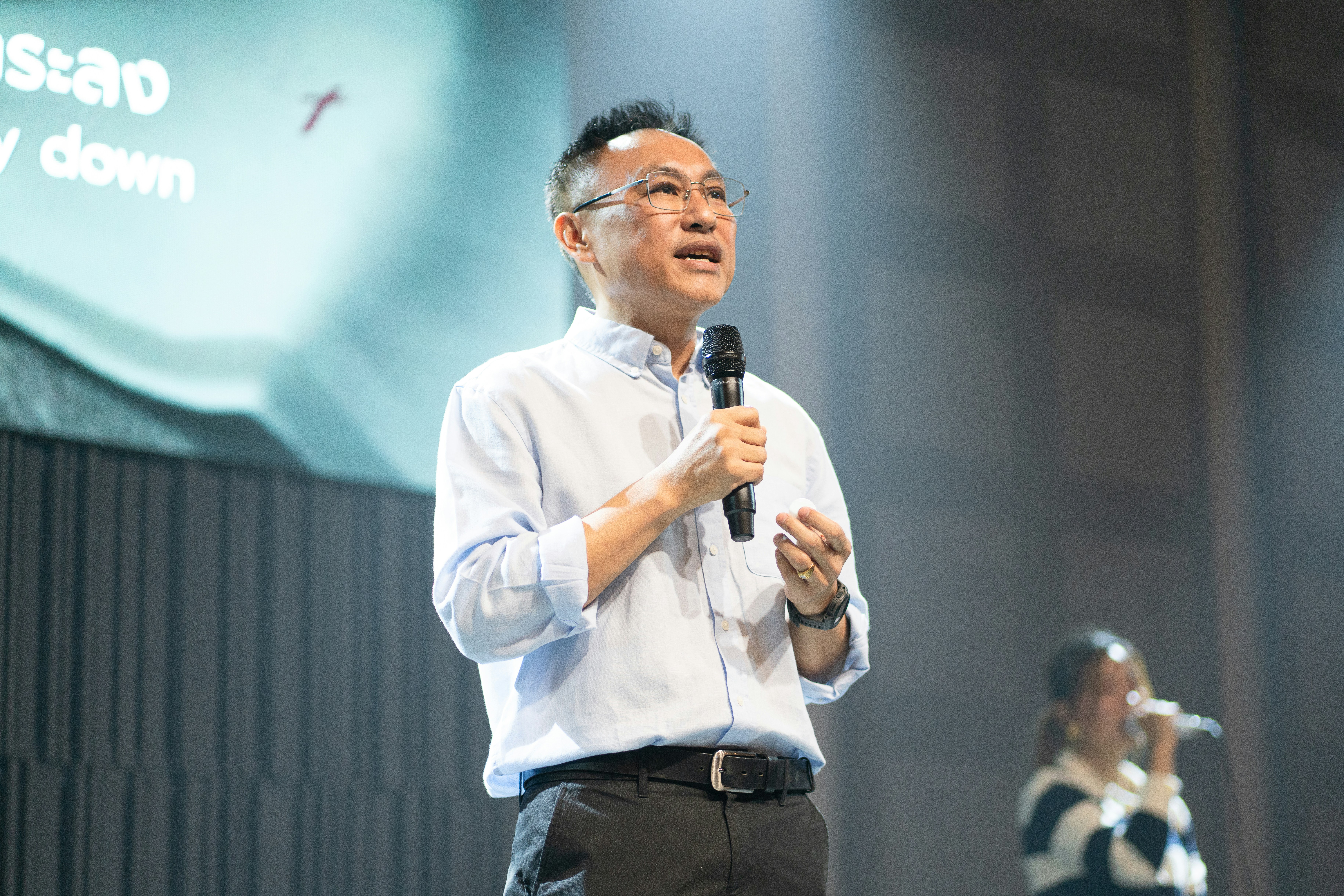 A man in a light blue shirt speaking into a microphone on stage.