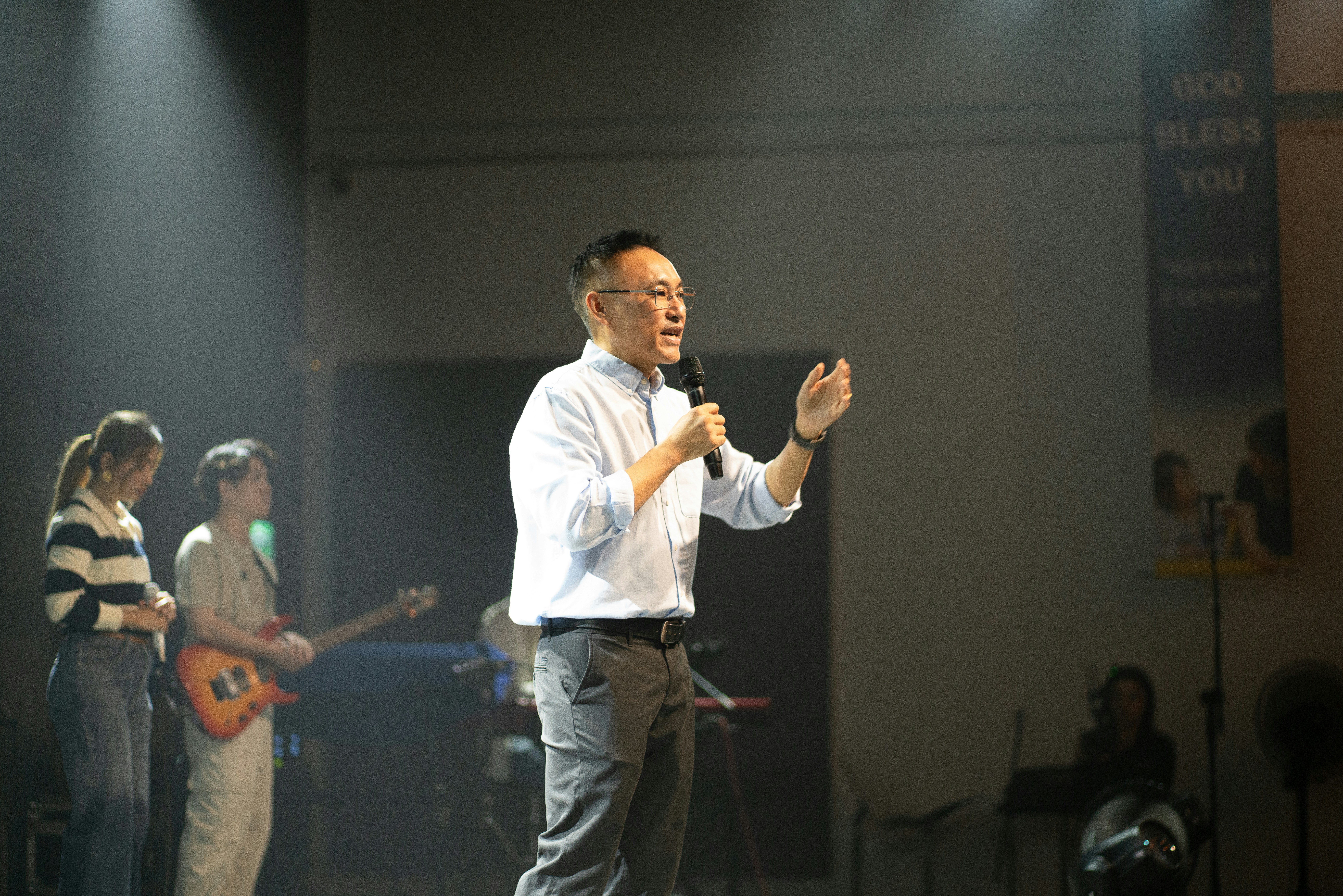A man speaking into a microphone on a stage with musicians behind him.