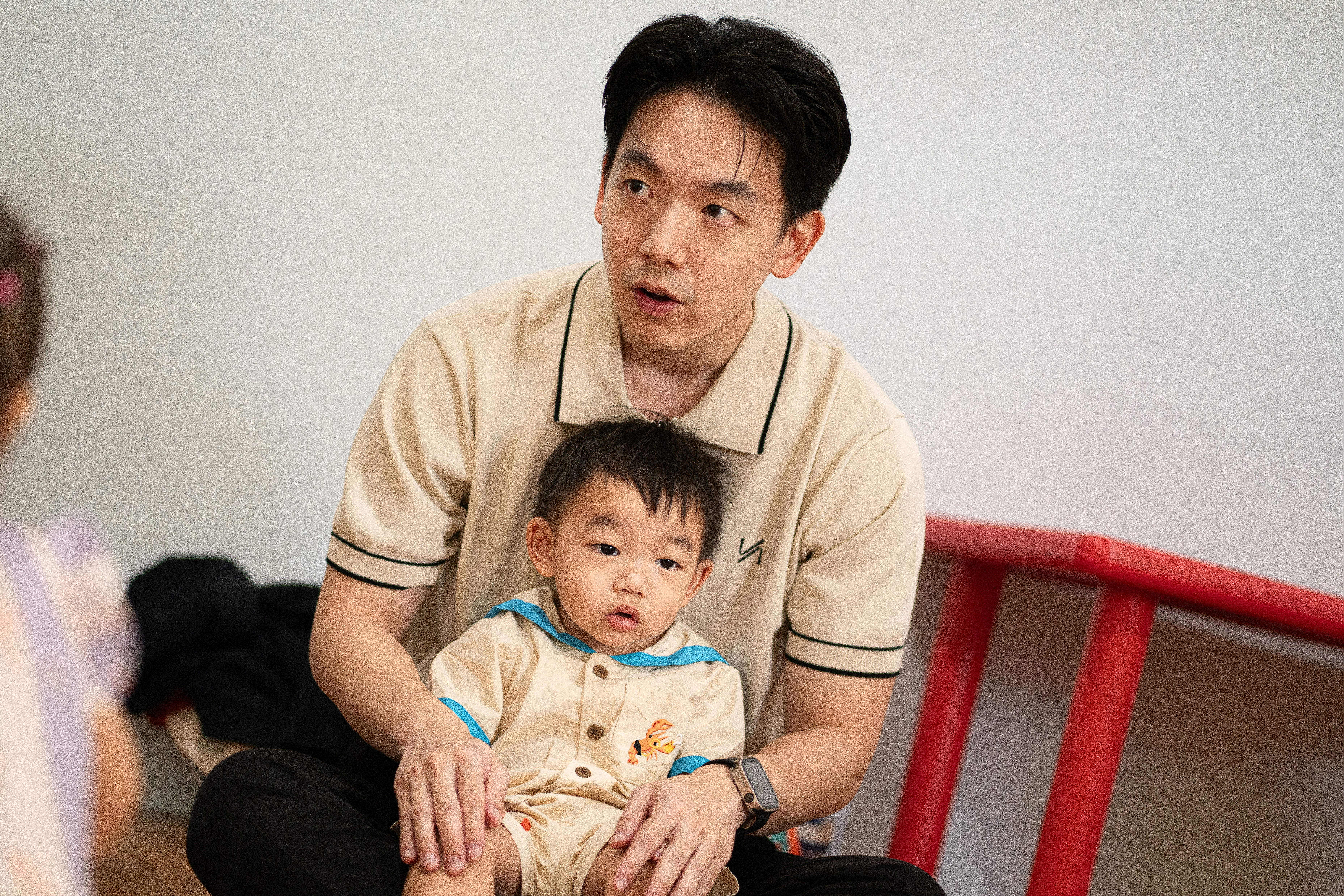An adult holding a baby on his lap in a bright room.