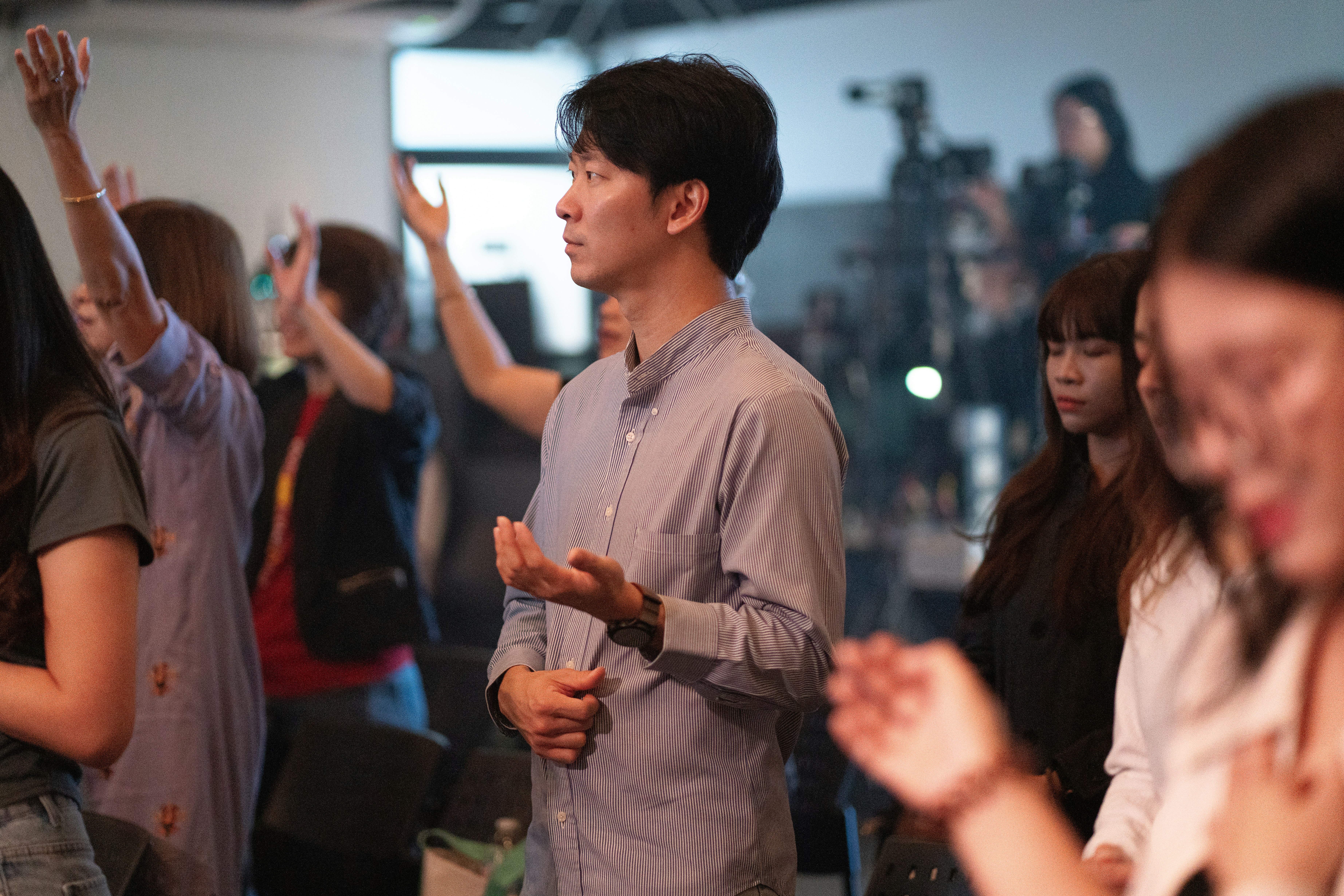 A group of people with hands raised in a dimly lit indoor gathering.