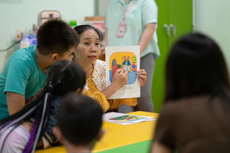 A woman pointing to an illustrated book for a group of children