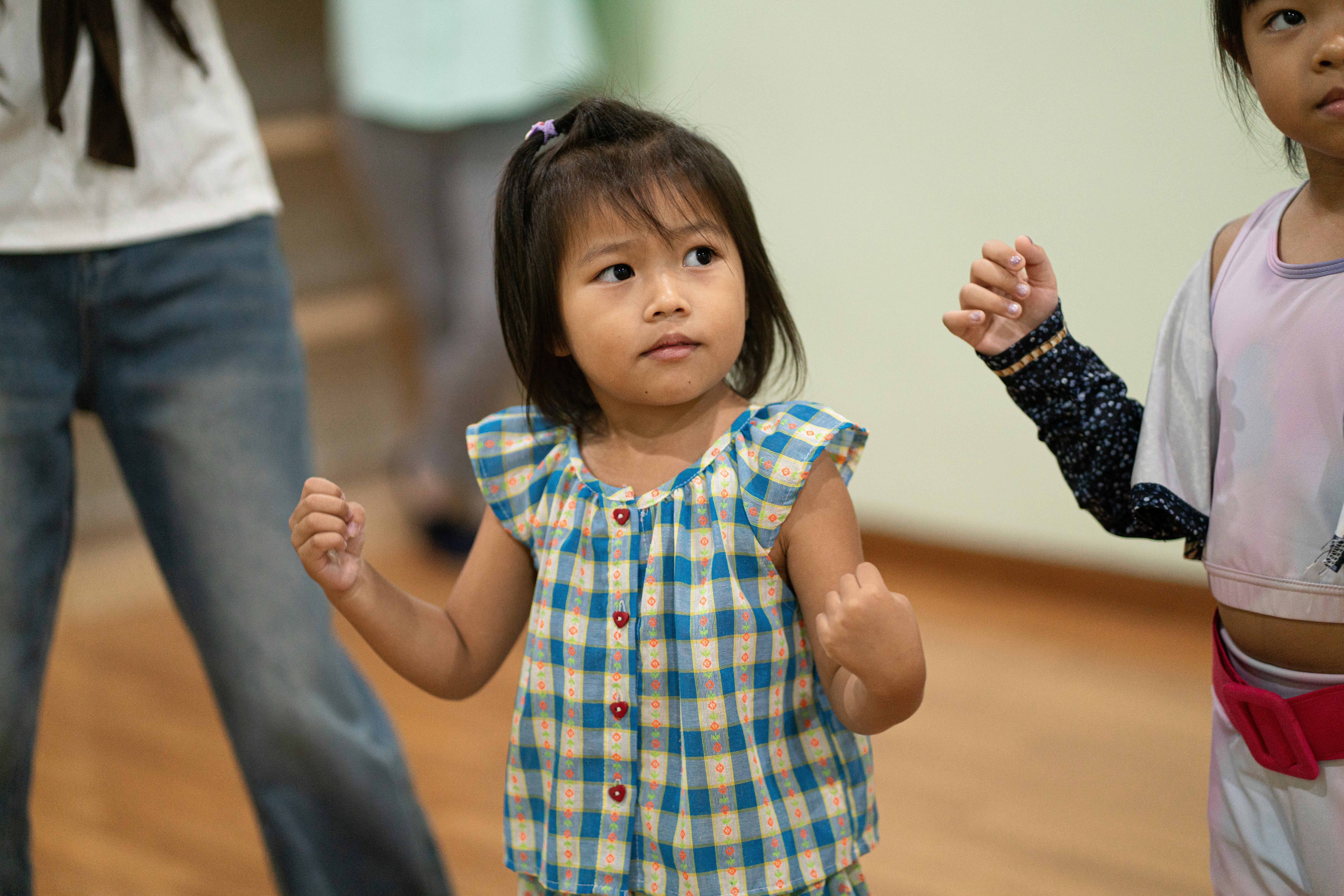 A young child in a blue plaid top dancing in a studio.