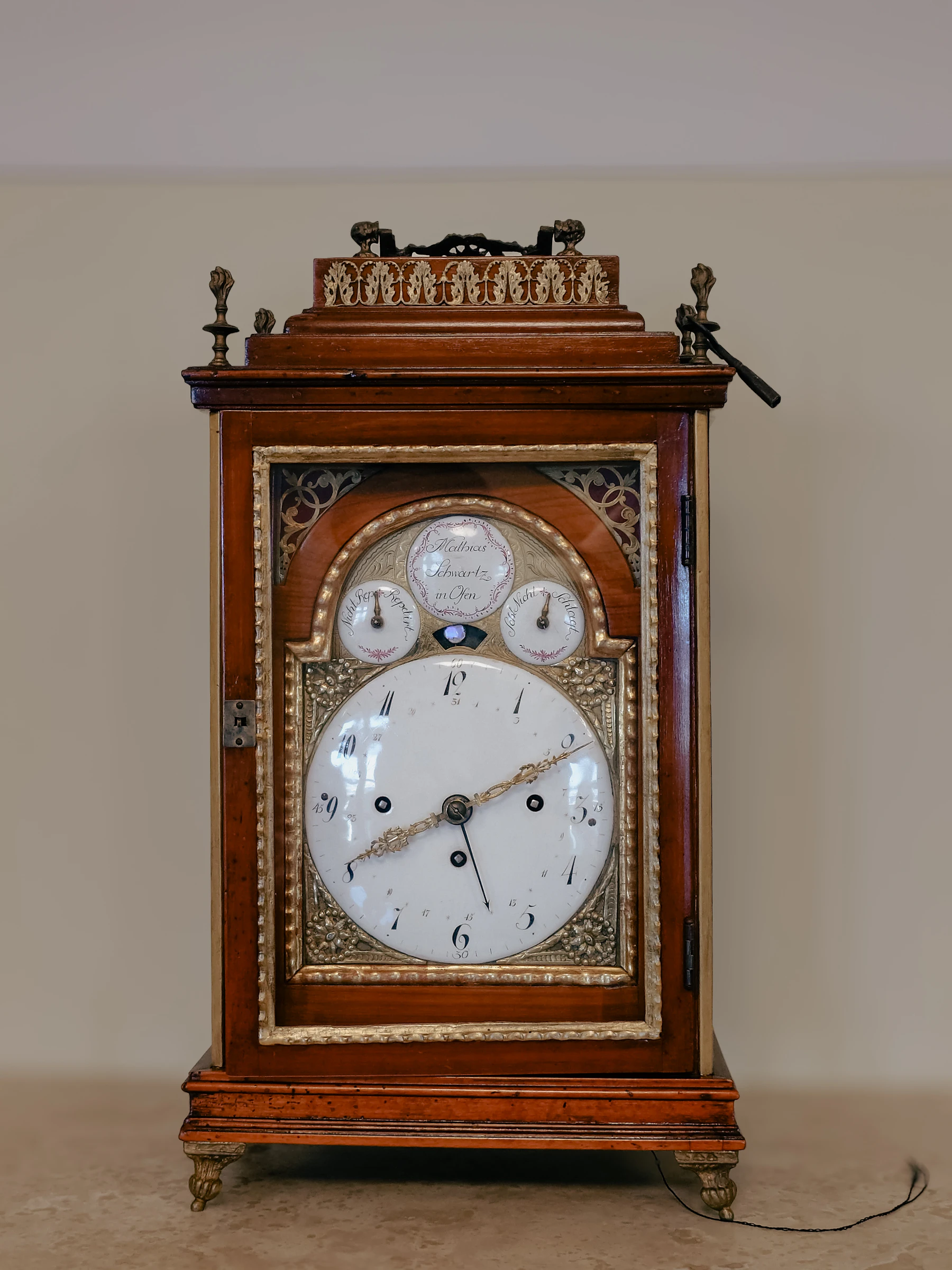 A wooden bracket clock with a white enamel dial, gilt mounts and a carrying handle, standing on a table