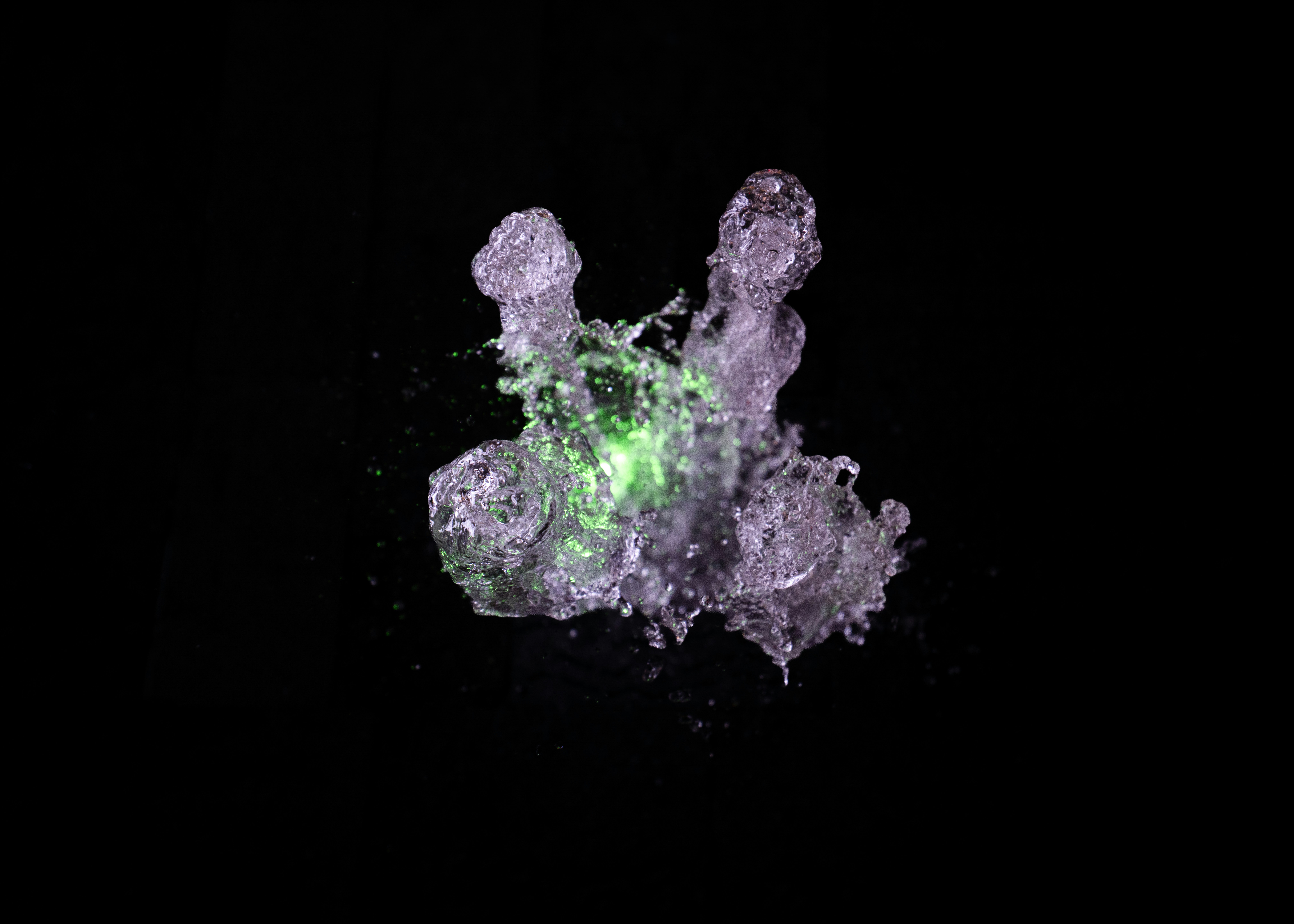 A splash of water illuminated by a bright green light against a black background.