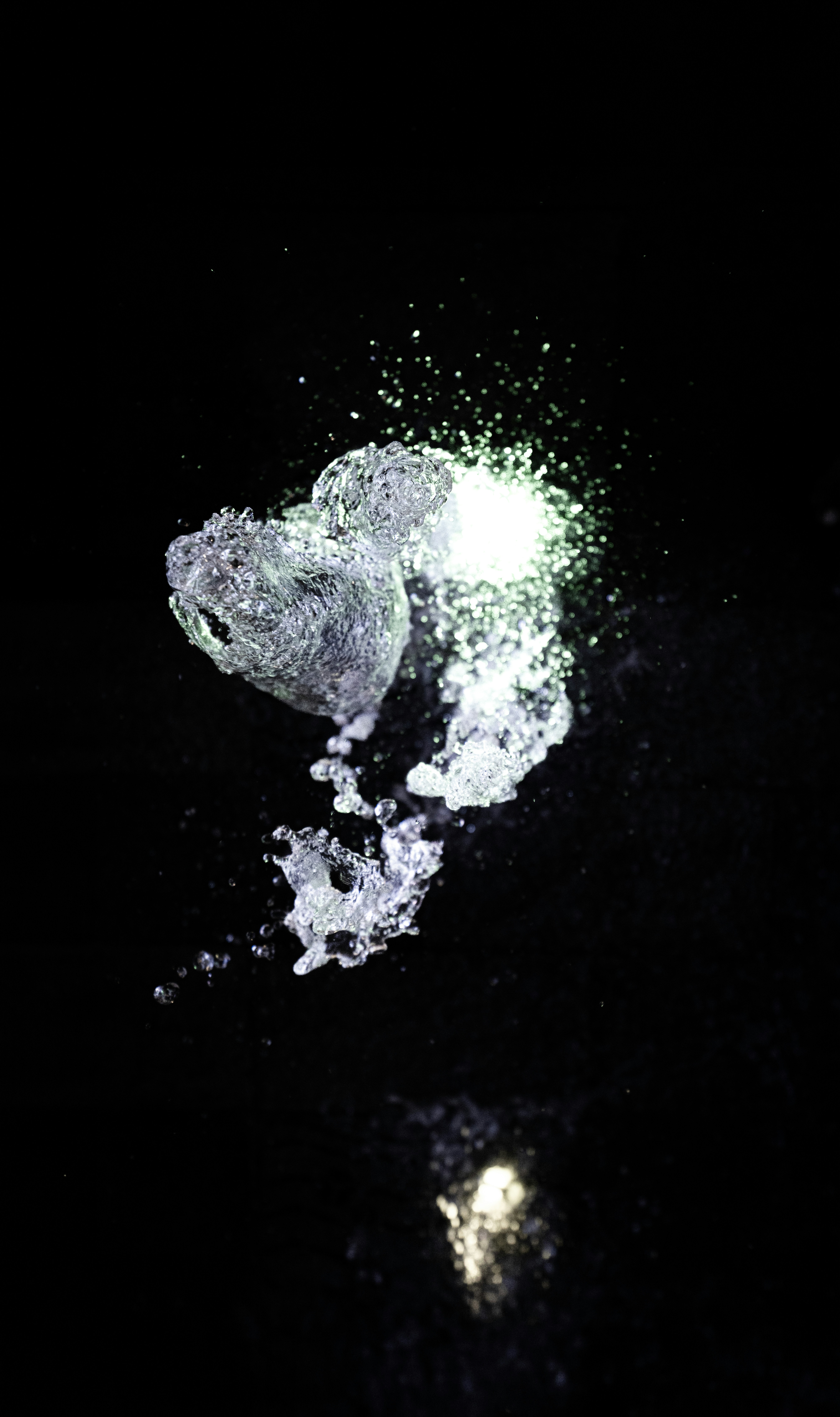 A splash of water illuminated by a bright green light against black.