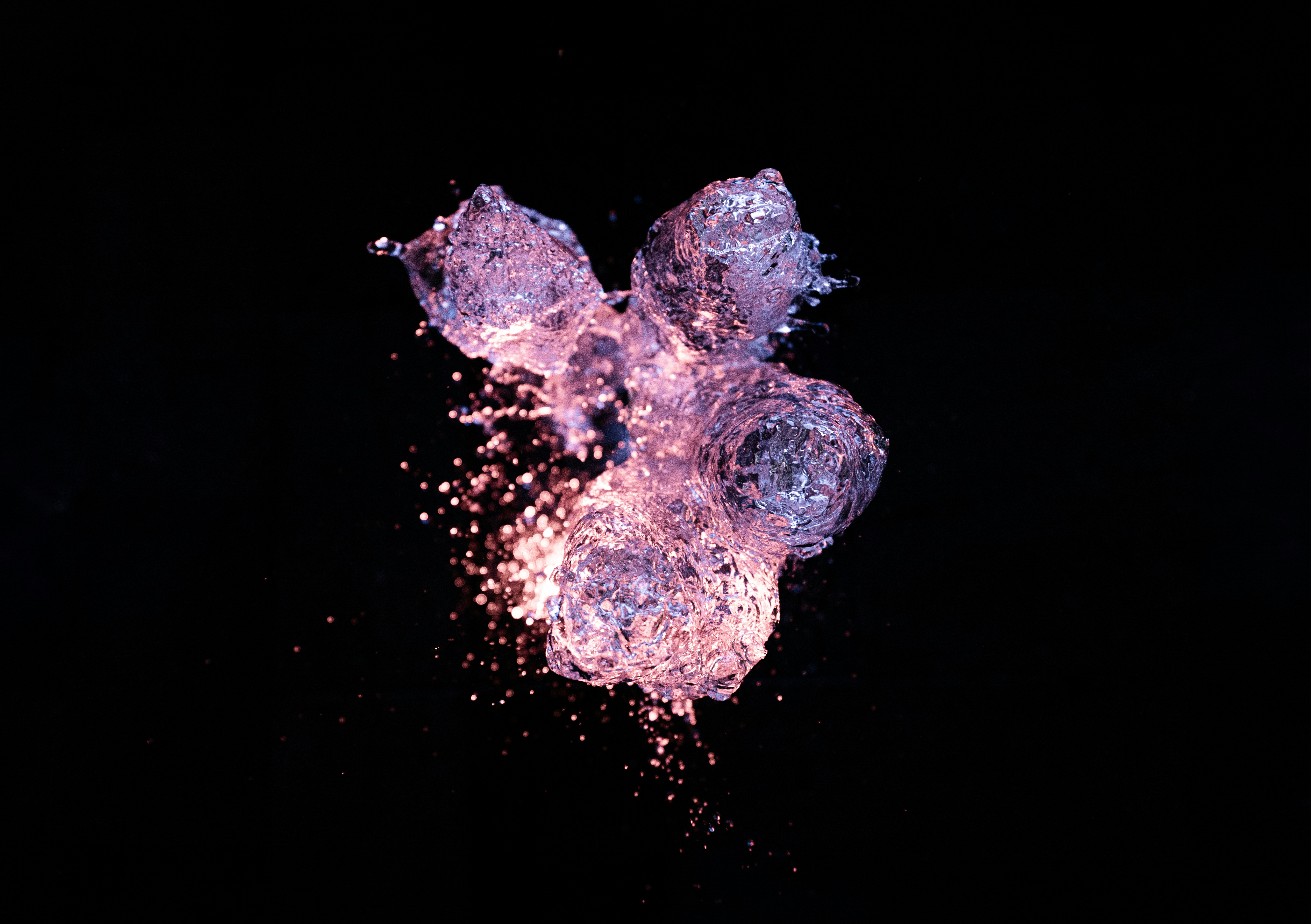 Splashing water droplets illuminated by pink light against a solid black background.
