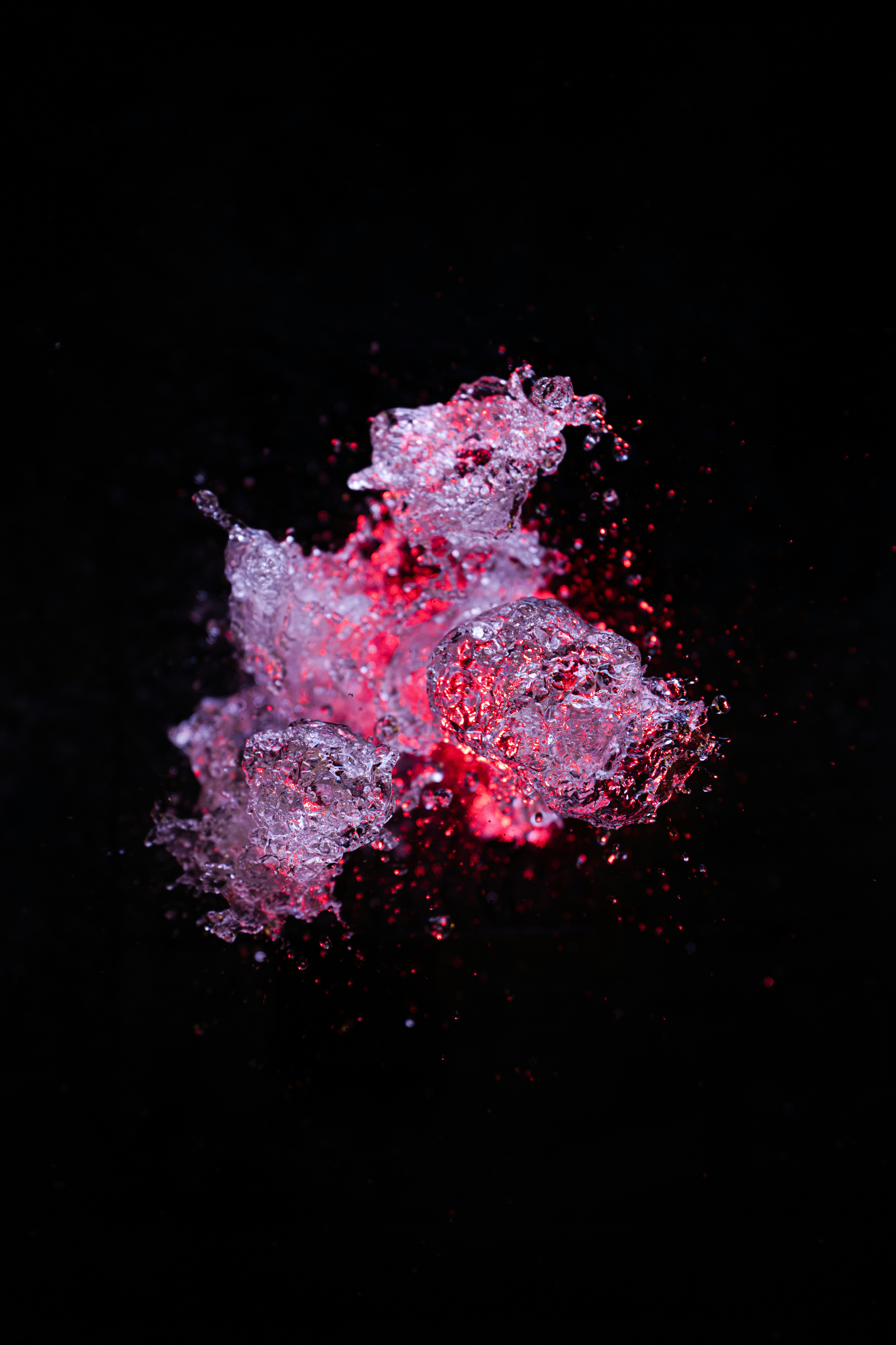 Splashing water droplets illuminated by a vibrant red light against a black background.